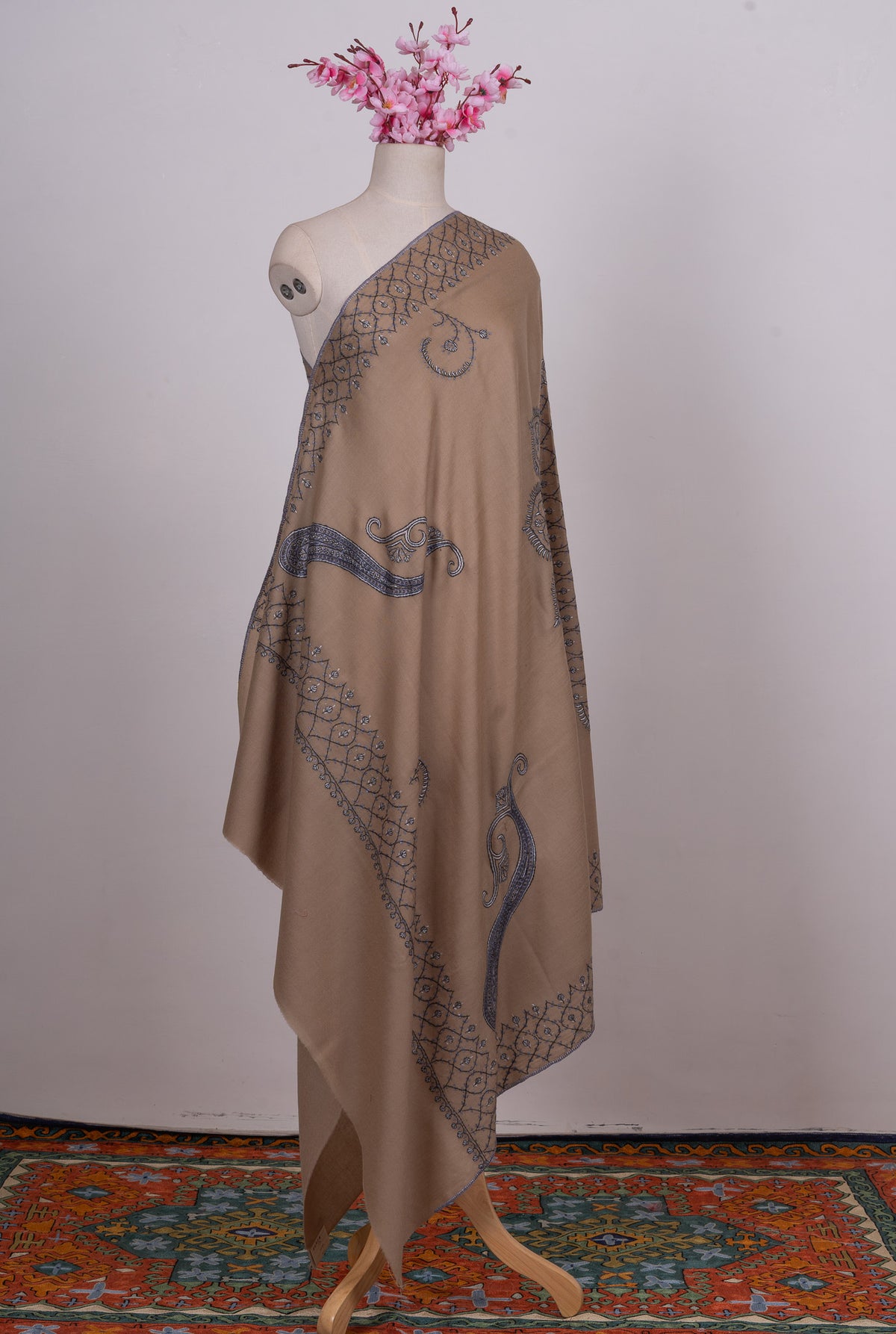 Full-length view of a desert-beige Merino wool shawl on a mannequin, with blue-grey paisleys, floral curls and lattice borders