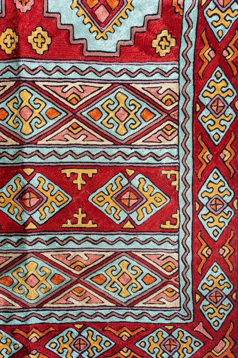 Close-up of the rug’s chain-stitch texture, with turquoise, yellow and pink diamonds outlined in black between zigzag borders