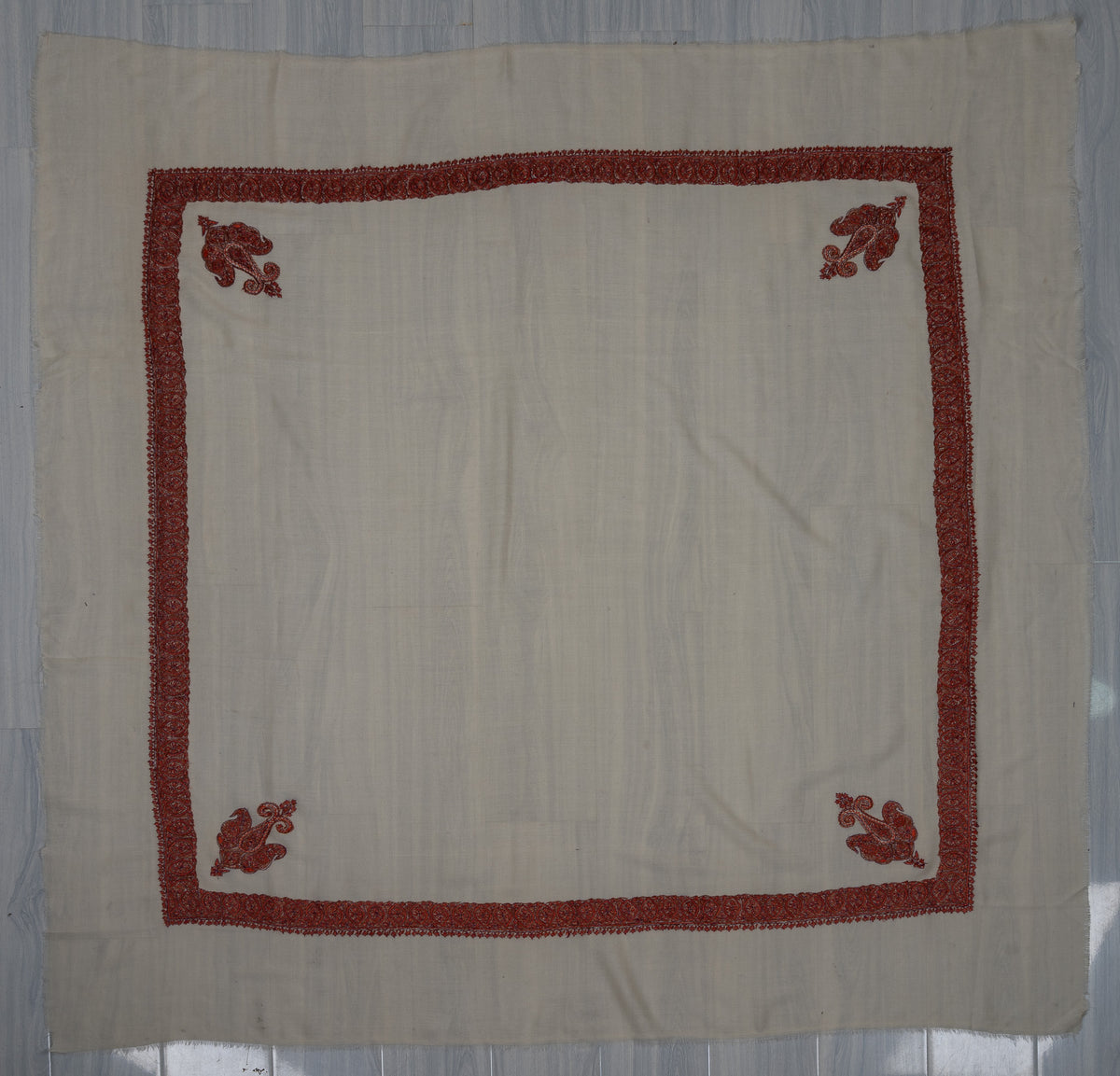 Square ivory rumal laid flat with four ruby-red Sozni corner paisleys, a narrow floral border and a plain centre