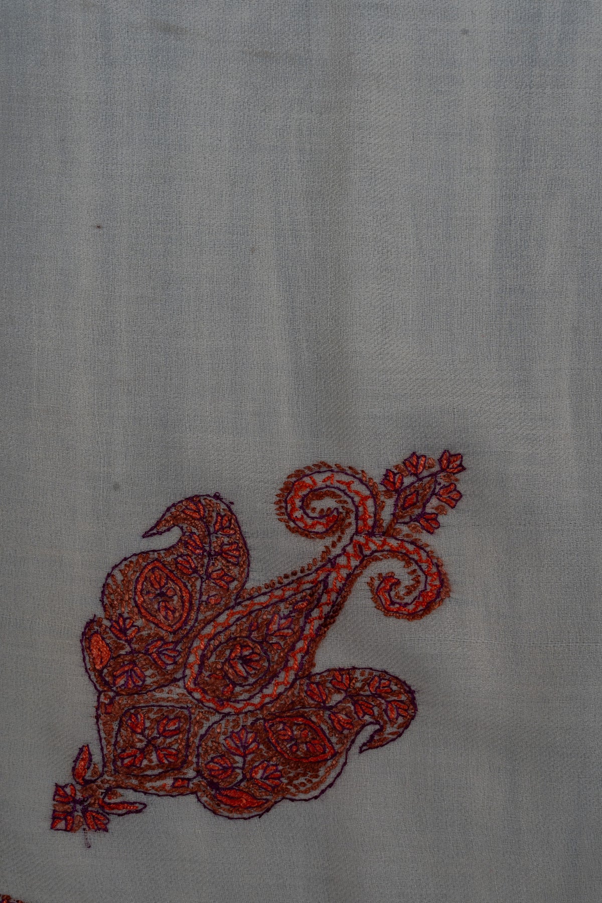 Close-up of a ruby-red Sozni paisley with curling tips and fine floral details on ivory rumal fabric