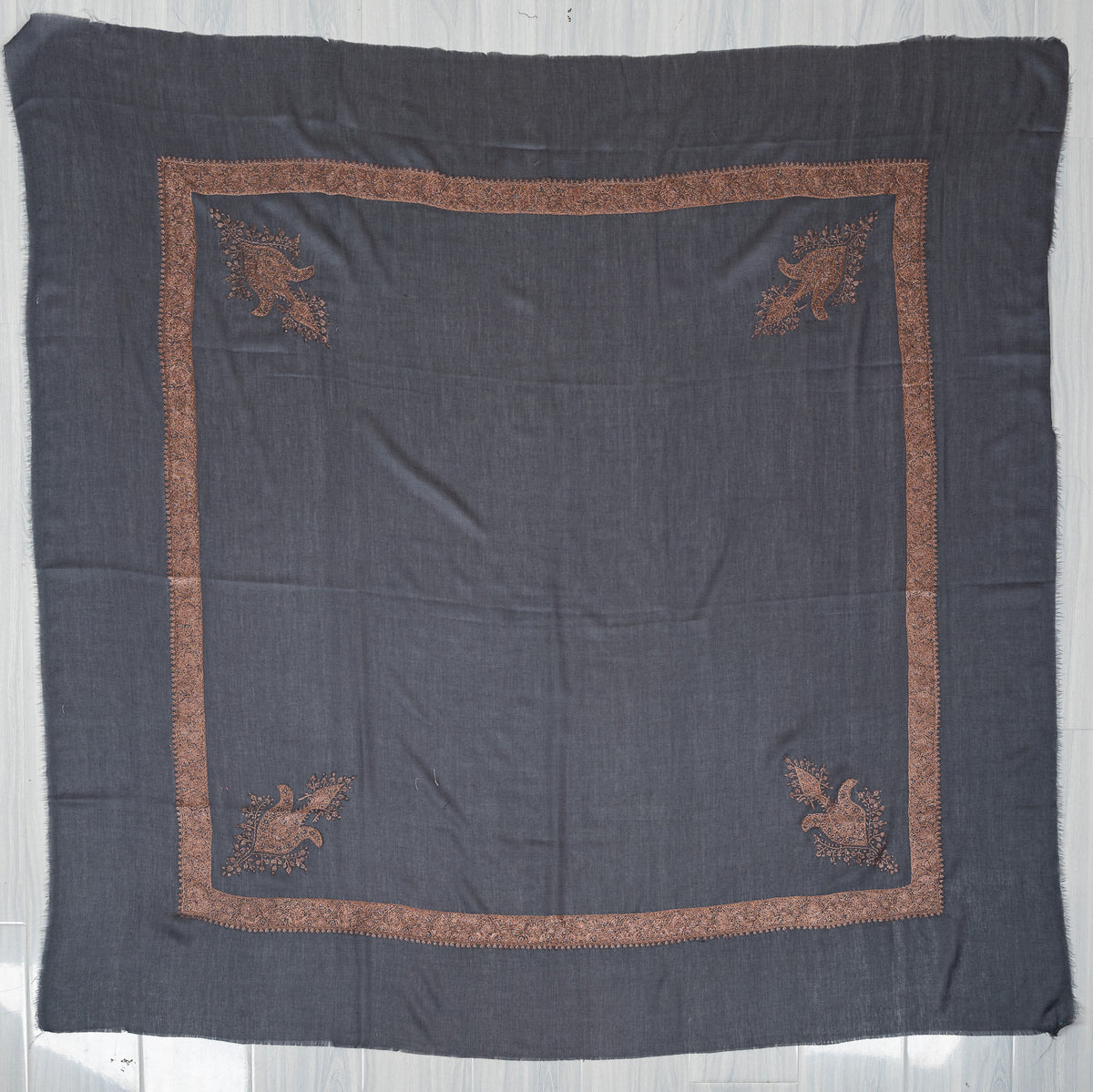Slate-blue square Merino wool rumal laid flat, with a copper-toned embroidered border and four ornate floral corner motifs