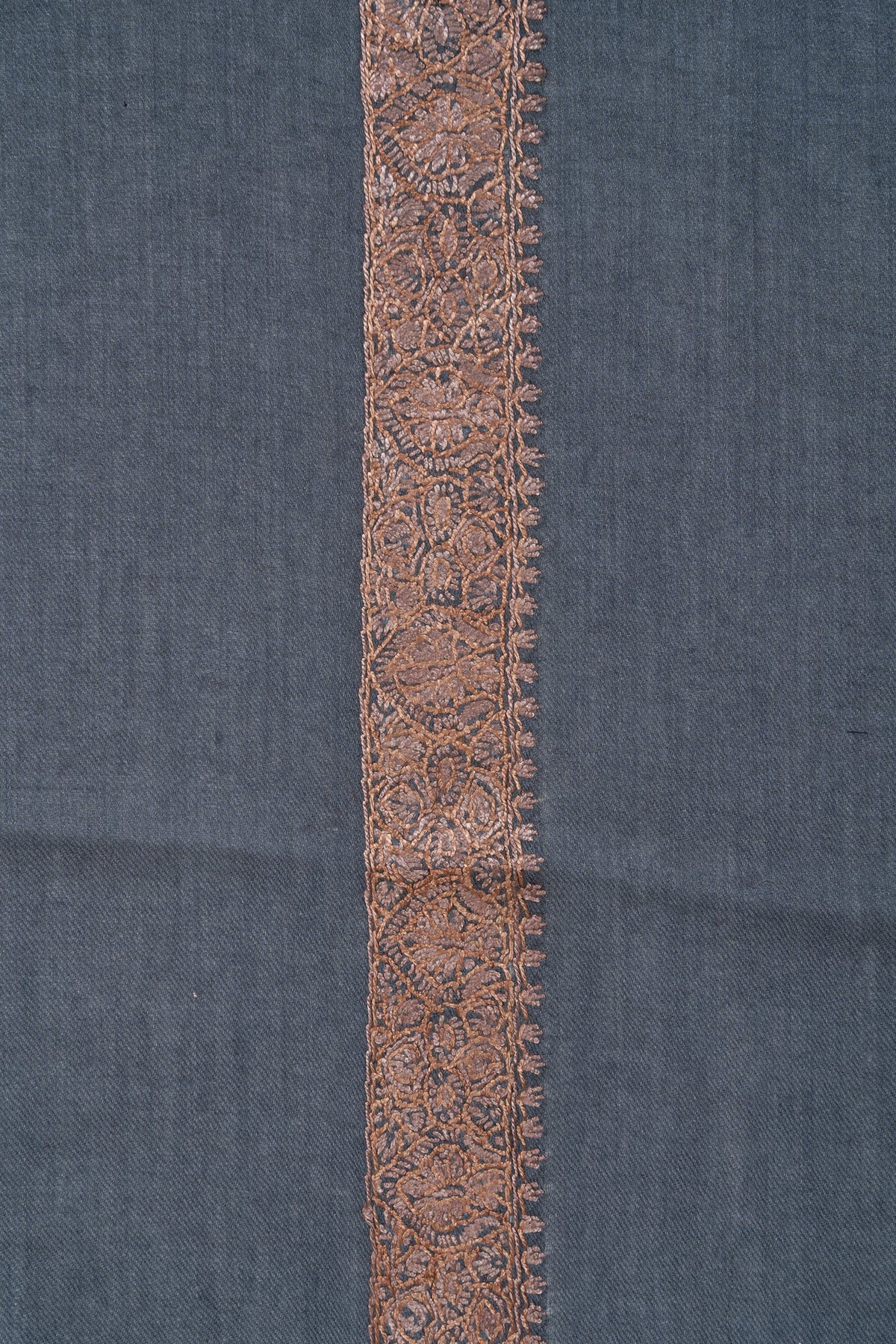 Close-up of a copper-toned Sozni border with dense floral stitching and tiny leafy edging on slate-blue rumal fabric