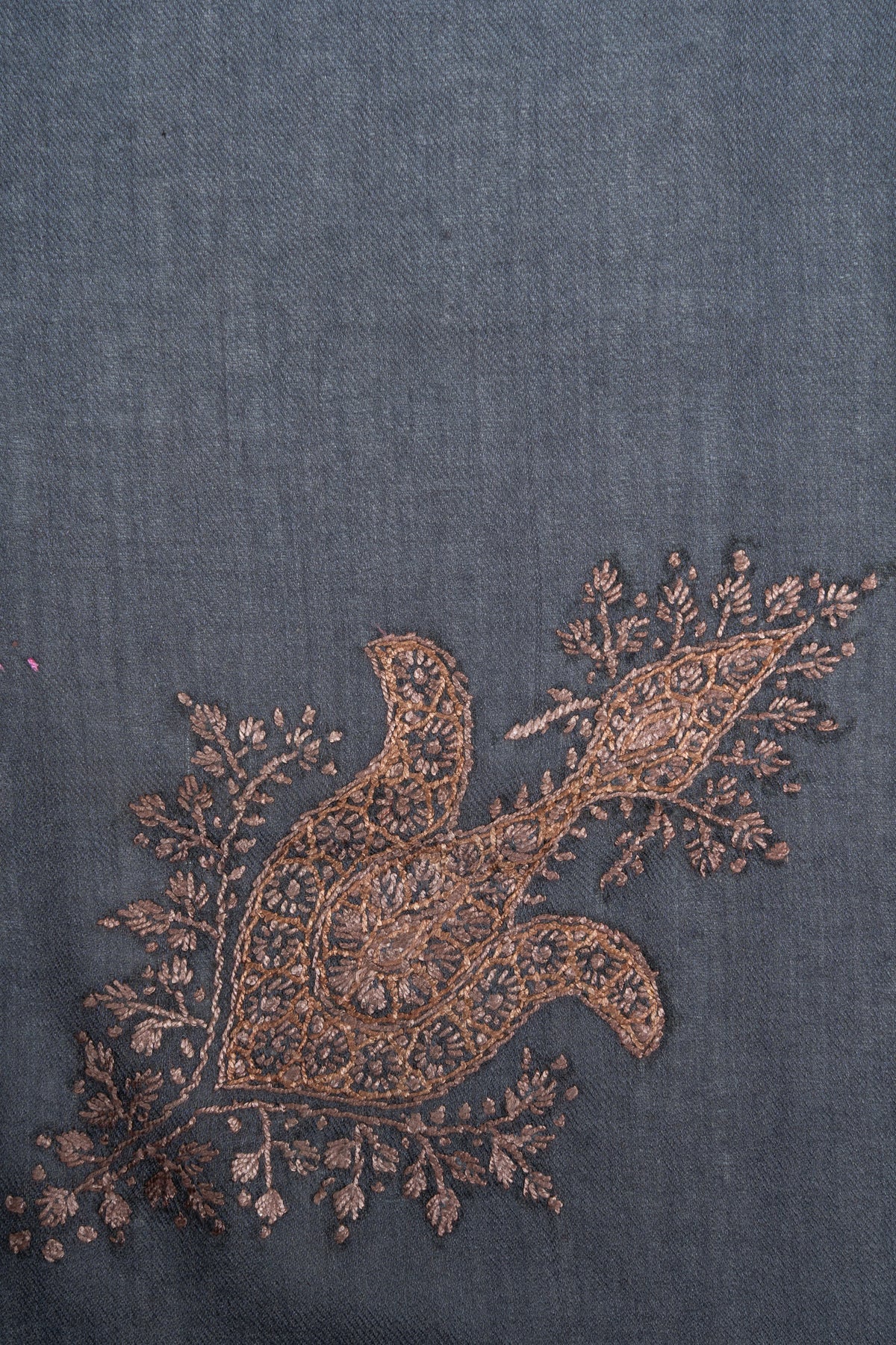 Close-up of an ornate copper-toned Sozni floral motif with curling lobes and delicate leafy sprays on slate-blue fabric