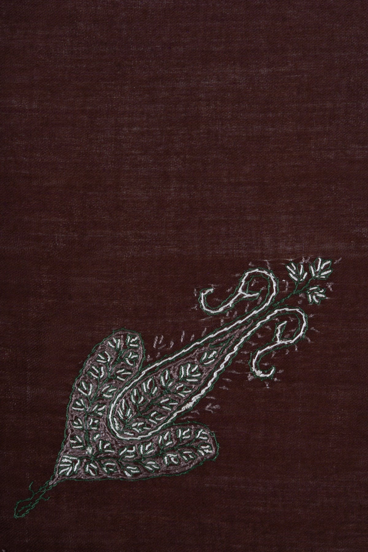Close-up of an elongated silver-grey Sozni paisley with curling tips and fine leaf details on chestnut-brown fabric