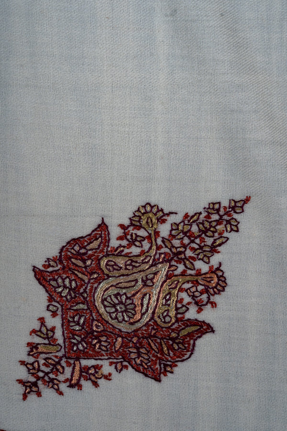 Close-up of an ornate crimson and gold Sozni motif with a teardrop centre and leafy sprays on ivory rumal fabric