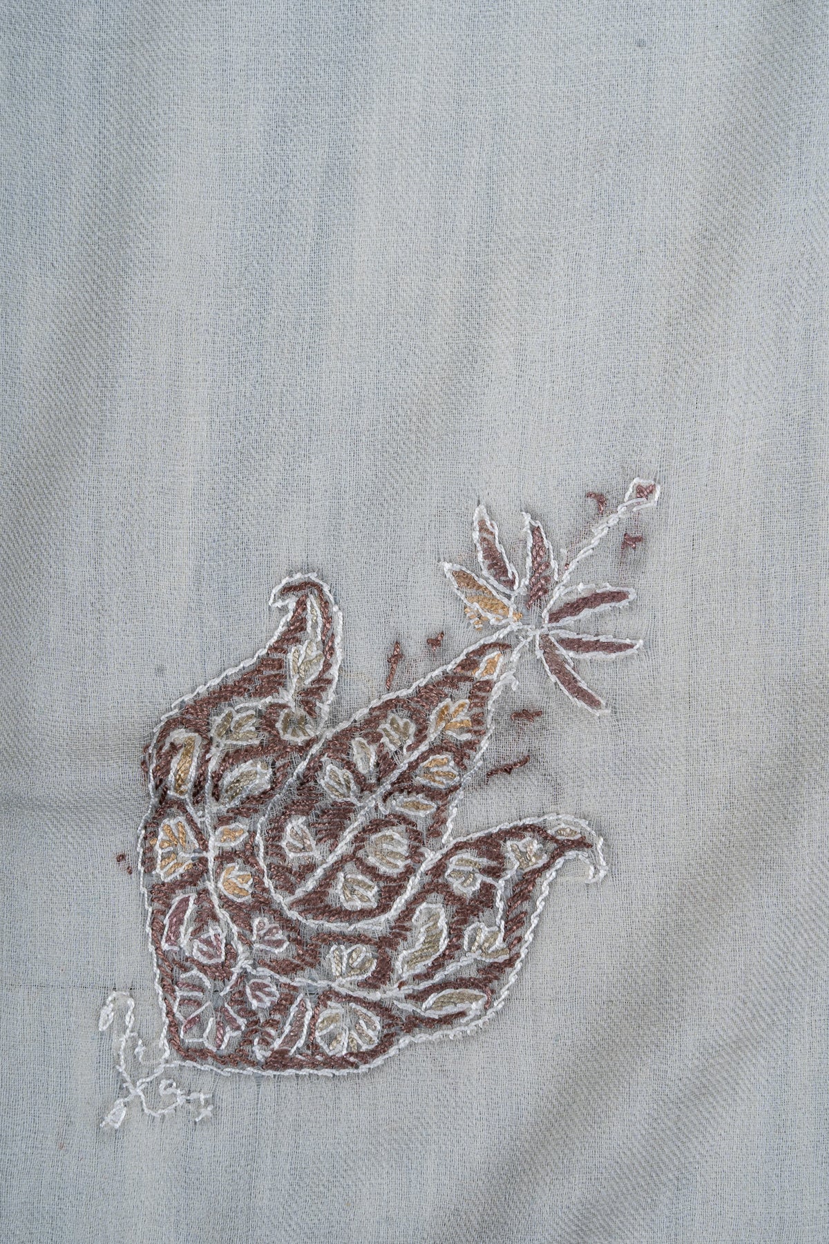 Close-up of a mocha and ivory Sozni floral motif with curling lobes, small leaves and a flower-tipped stem