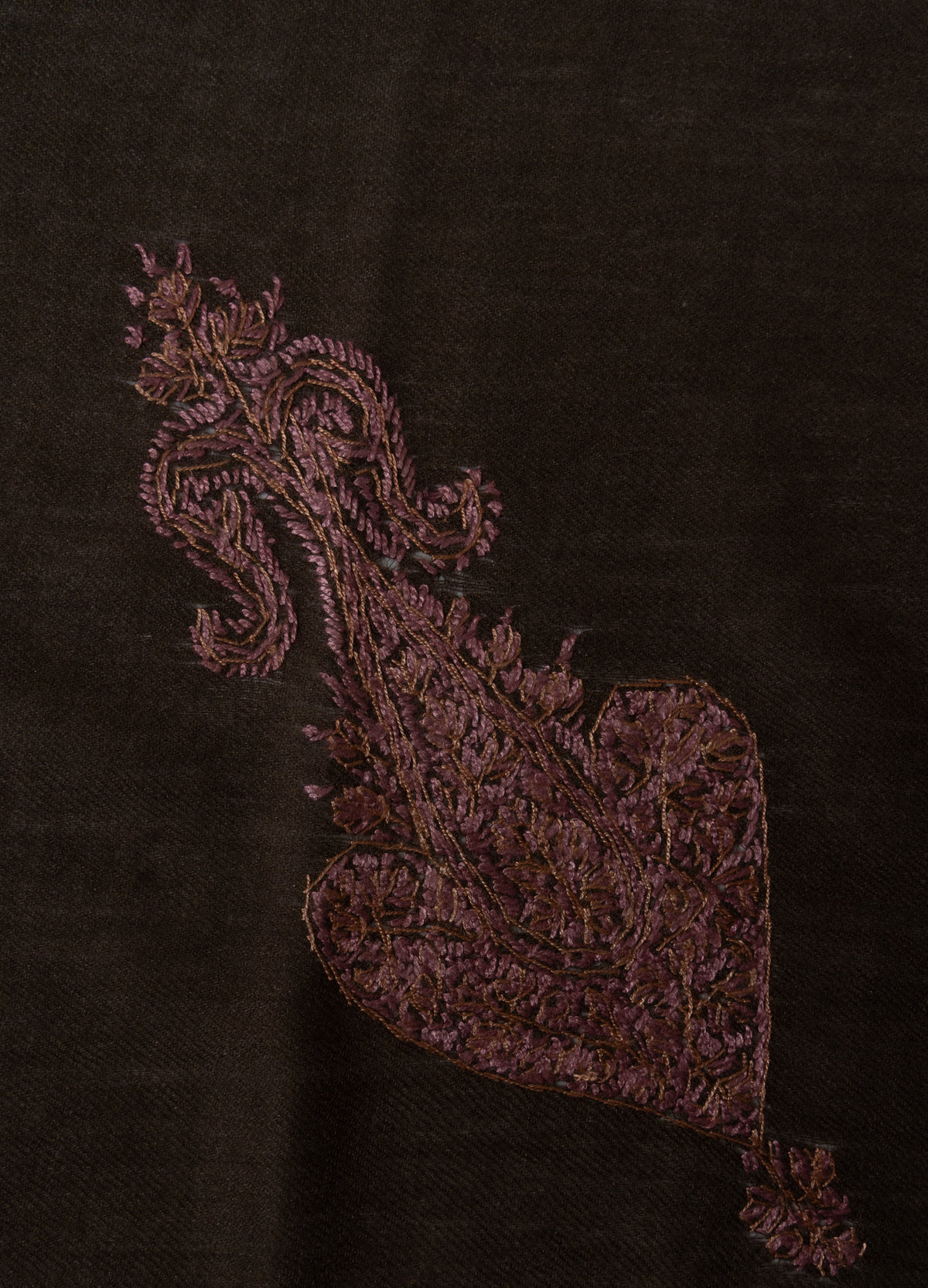 Close-up of an elongated dusty rose Sozni motif with fine flowers, leaves and curling tendrils on cocoa-brown fabric