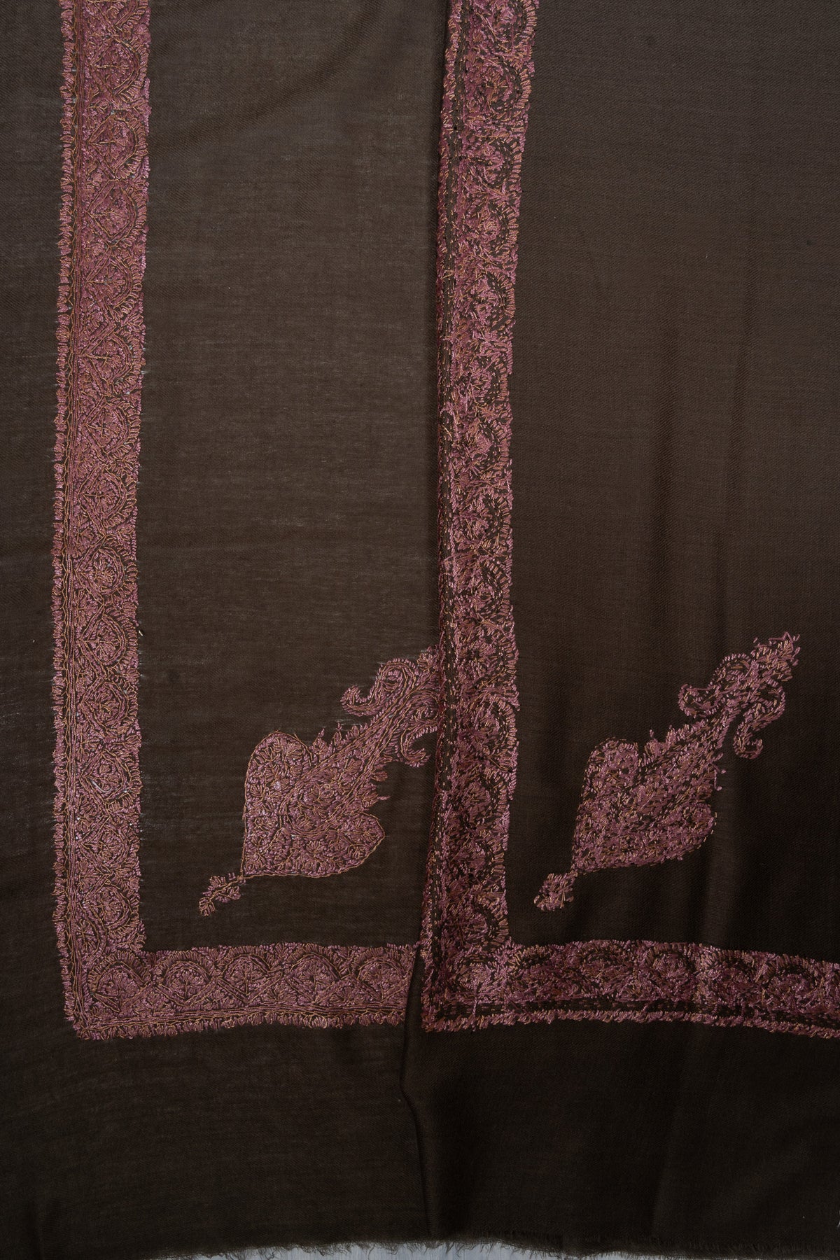 Overlapping corners of a dark brown Merino wool rumal showing rose-gold Sozni paisleys and floral borders.