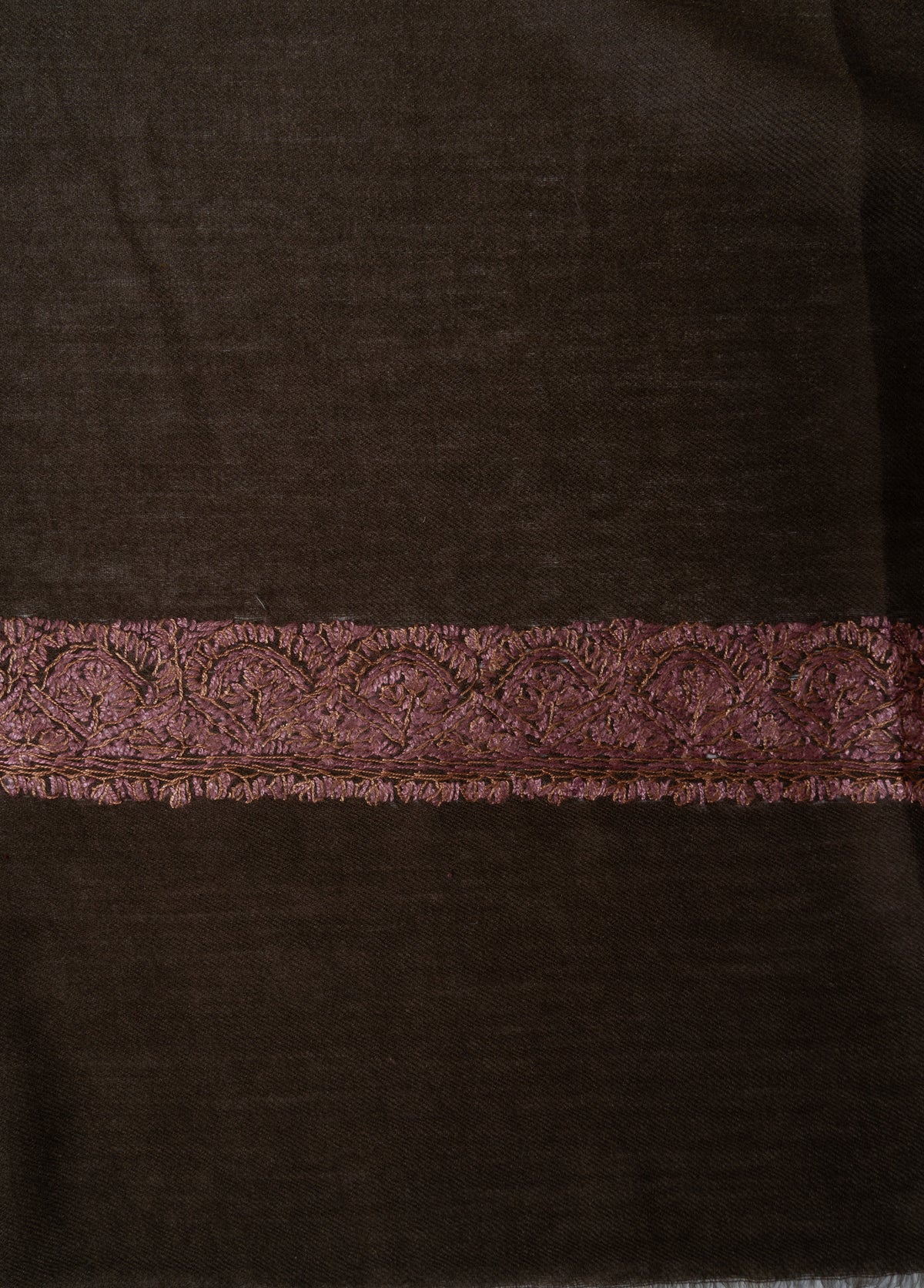 Close-up of a rose-gold Sozni floral border and fine leaf edging on dark brown Merino wool.