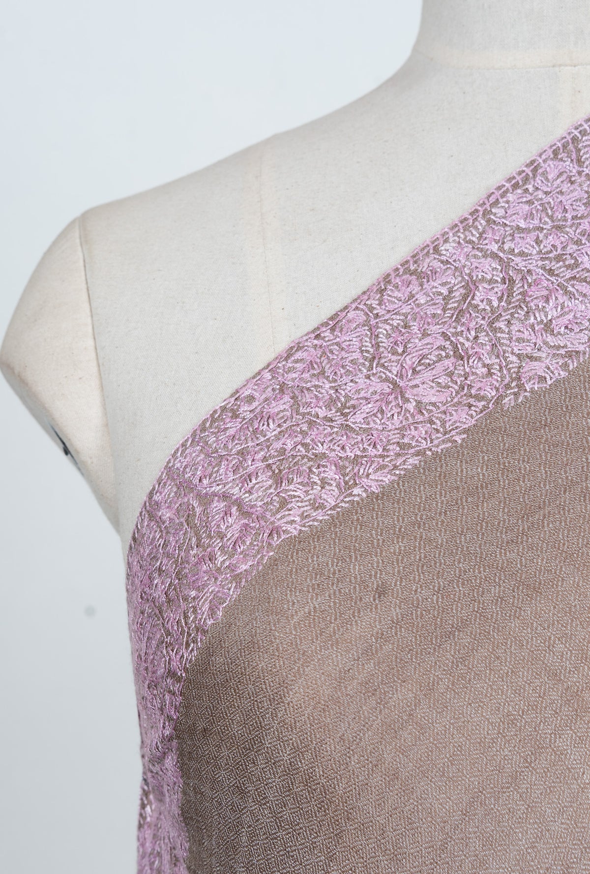 Shoulder detail showing blush-pink Sozni flowers and curling leaves on a taupe Merino wool shawl.