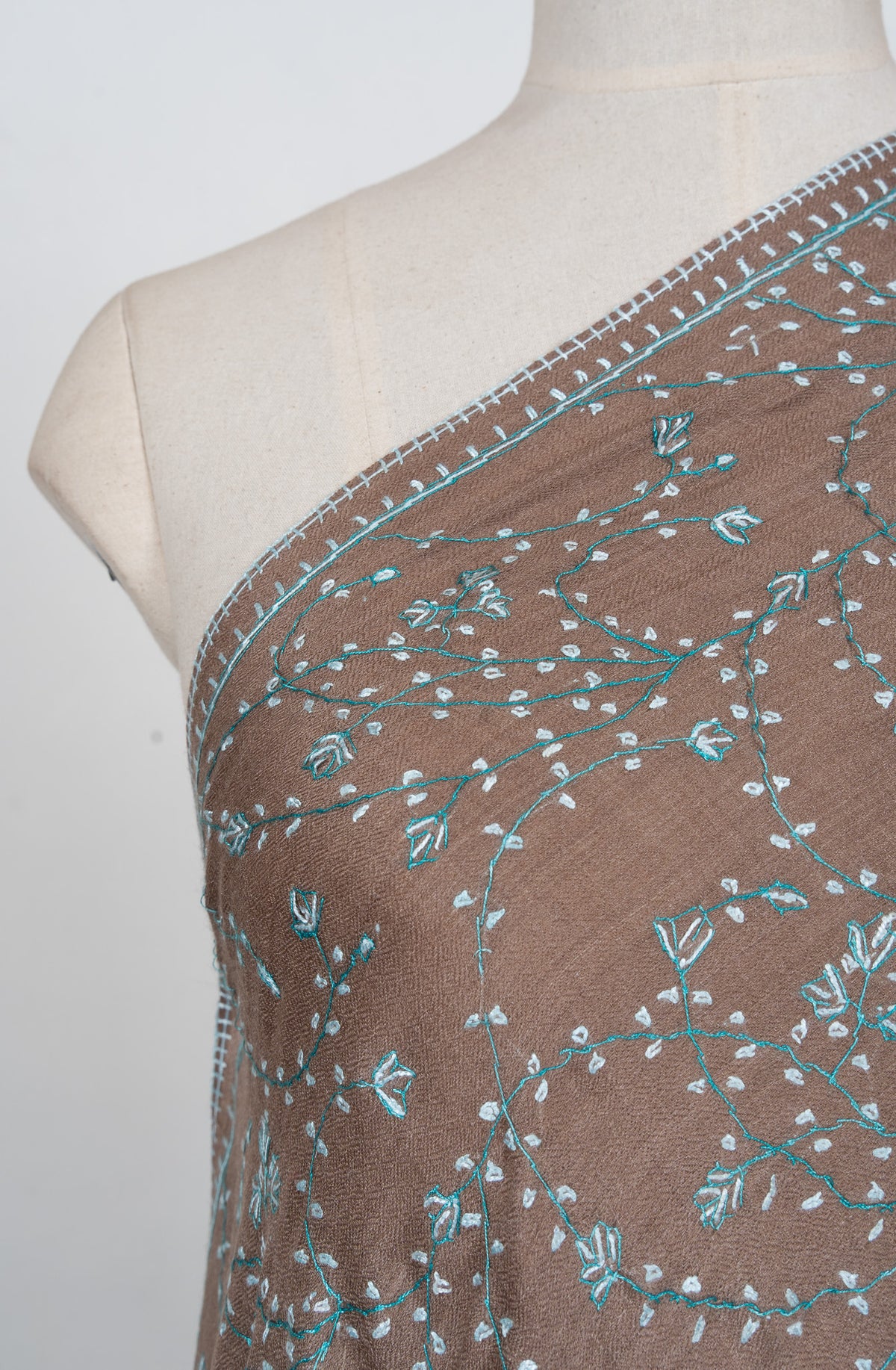 Shoulder detail of a cocoa-brown shawl showing pale aqua Sozni stems, tiny leaves and small floral clusters