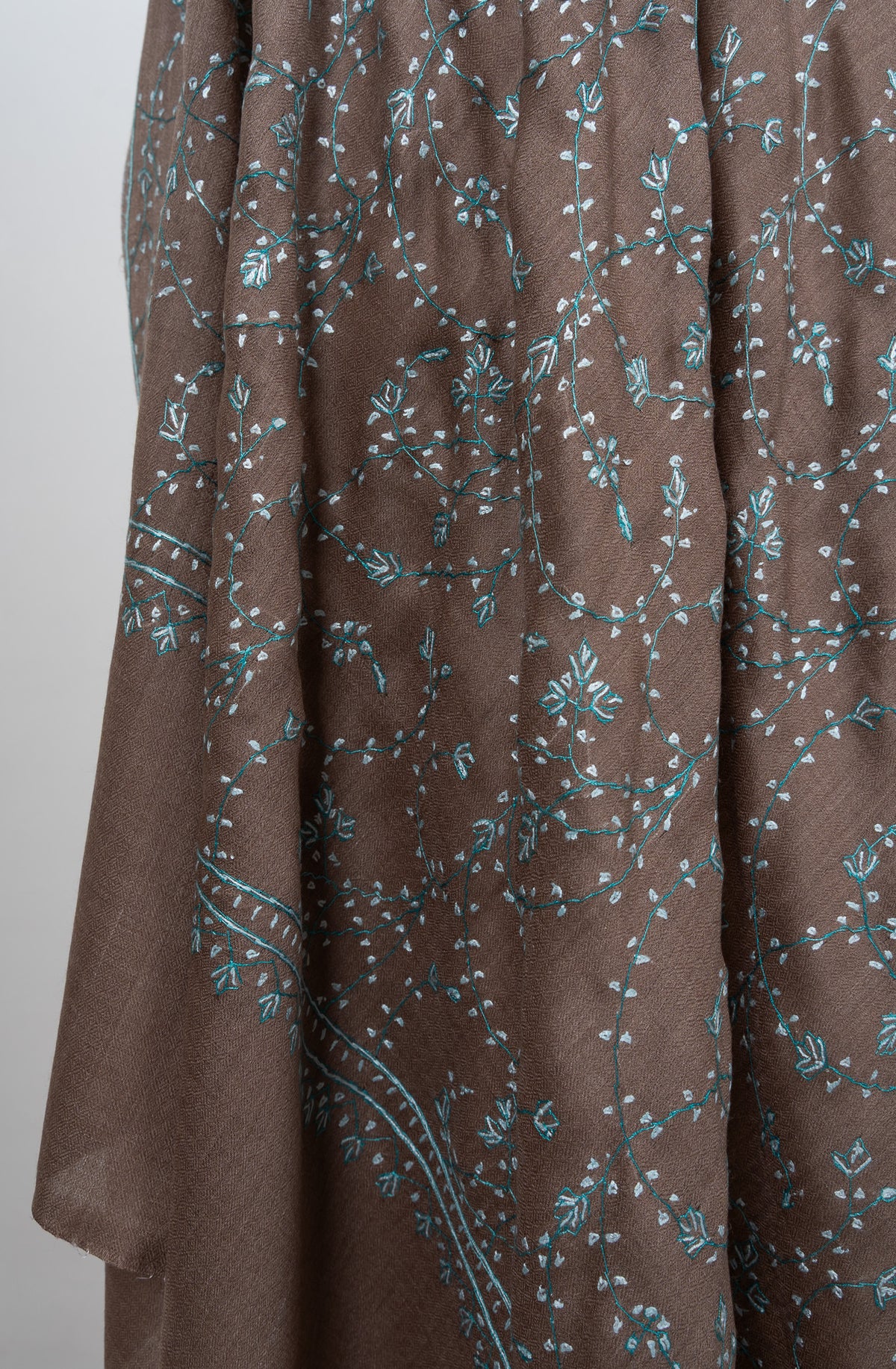 Folds of a cocoa-brown shawl showing pale aqua Sozni vines above a narrow embroidered border and plain end band