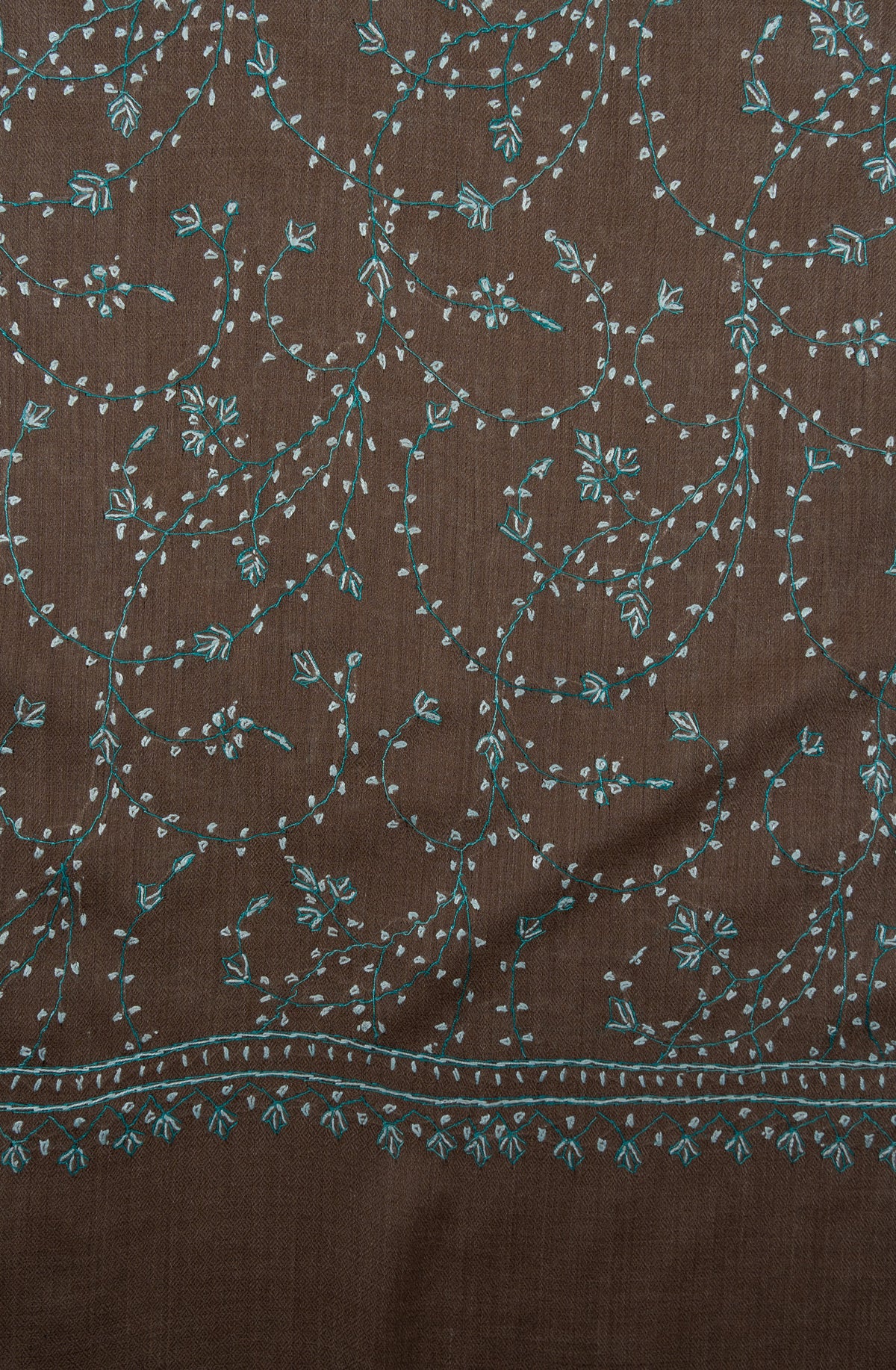 Close-up of pale aqua Sozni vines and small leaf motifs above the narrow end border of a cocoa-brown shawl