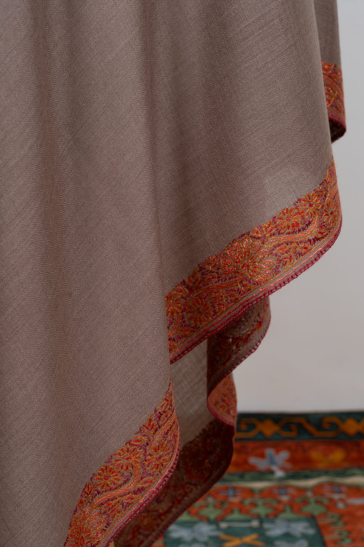 Truffle-brown shawl folds showing rust-orange embroidered borders around the plain fabric