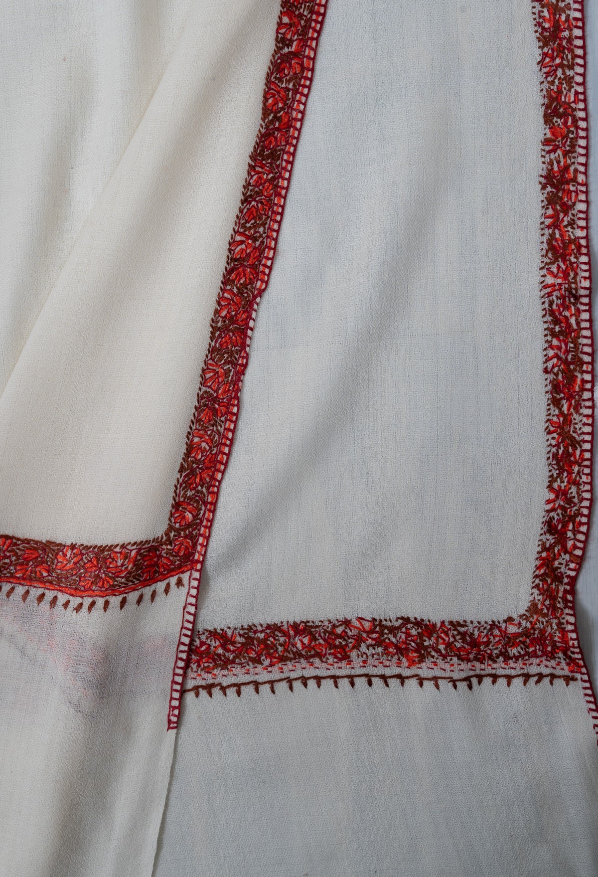 Folded ivory shawl corner showing both sides of narrow ember-red Sozni floral borders