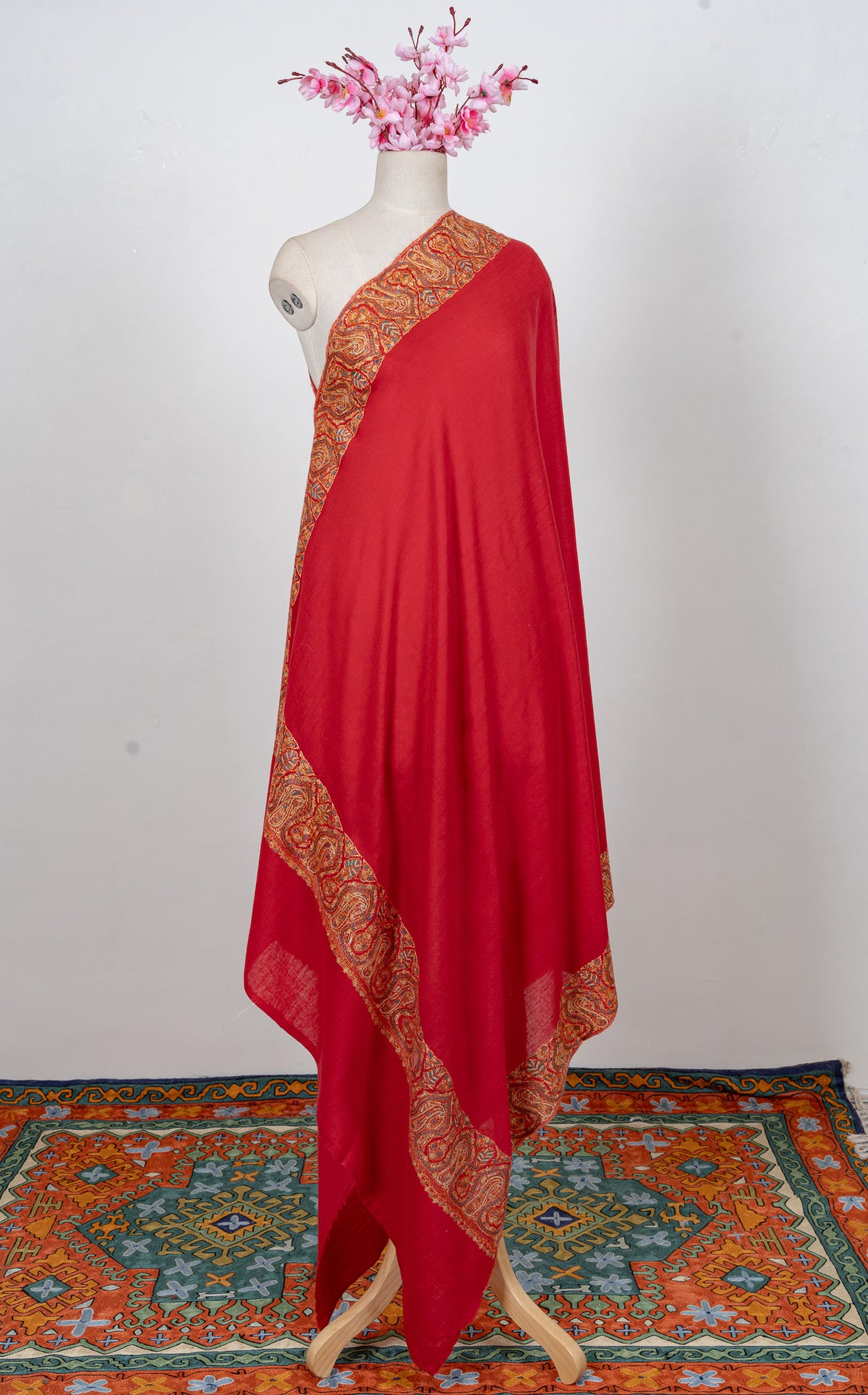 Full-length view of a scarlet merino wool shawl draped on a mannequin, with broad golden Sozni paisley borders