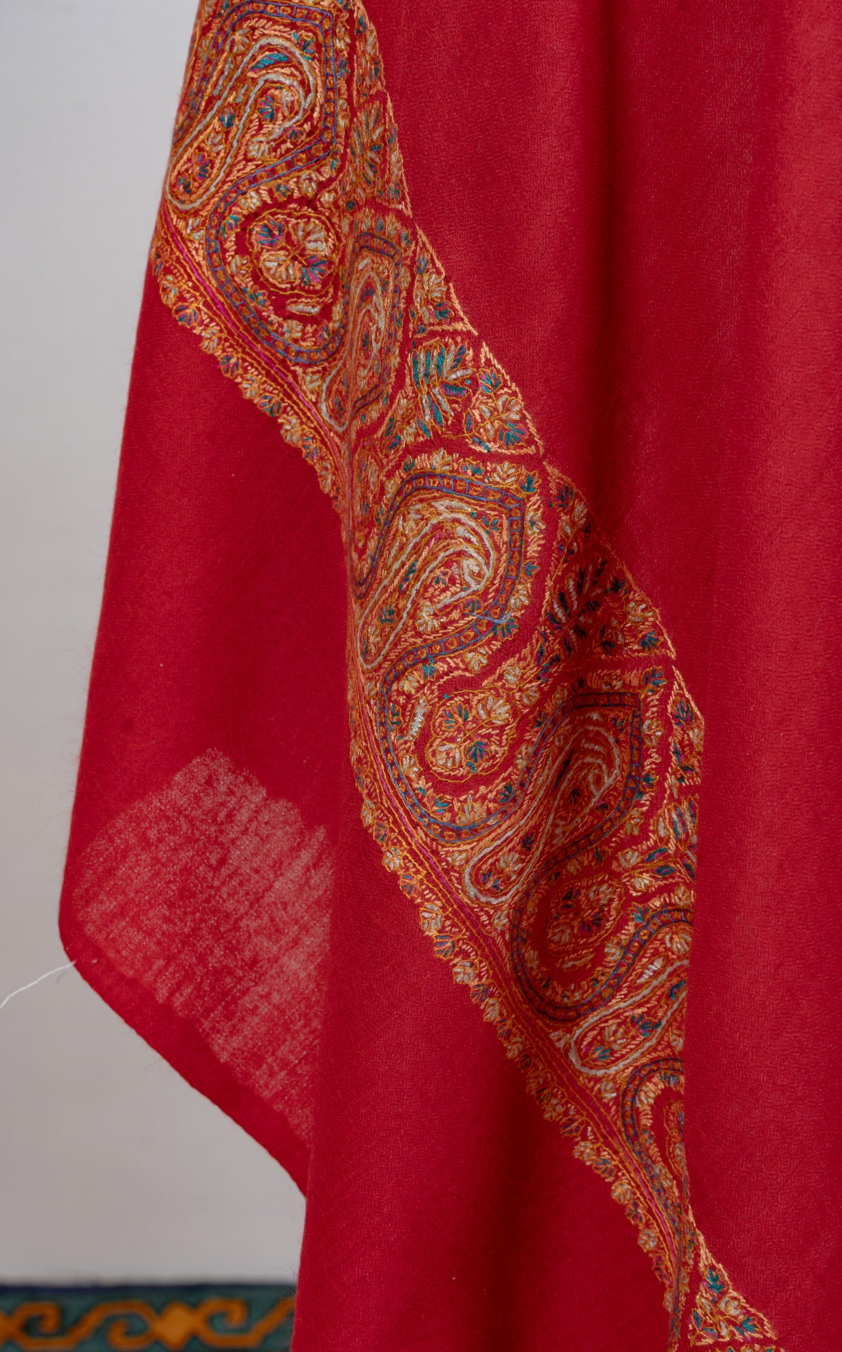 Scarlet shawl hanging in folds, showing its broad gold, blue and green Sozni paisley border