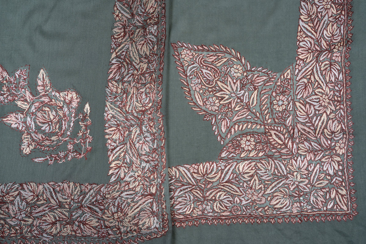 Folded sage-green rumal showing two contrasting corner motifs and overlapping cream-brown floral borders
