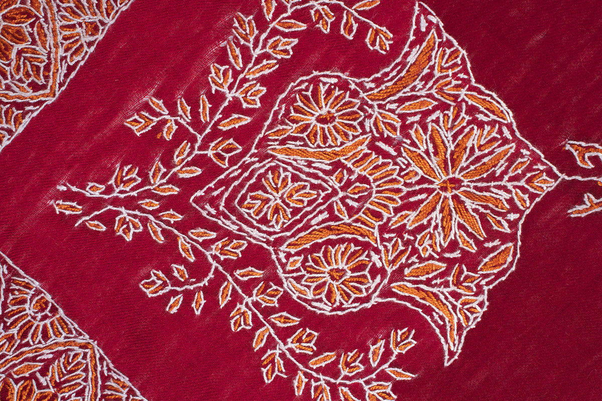 Close-up of a gold-and-ivory floral medallion with curling leafy stems embroidered on crimson fabric