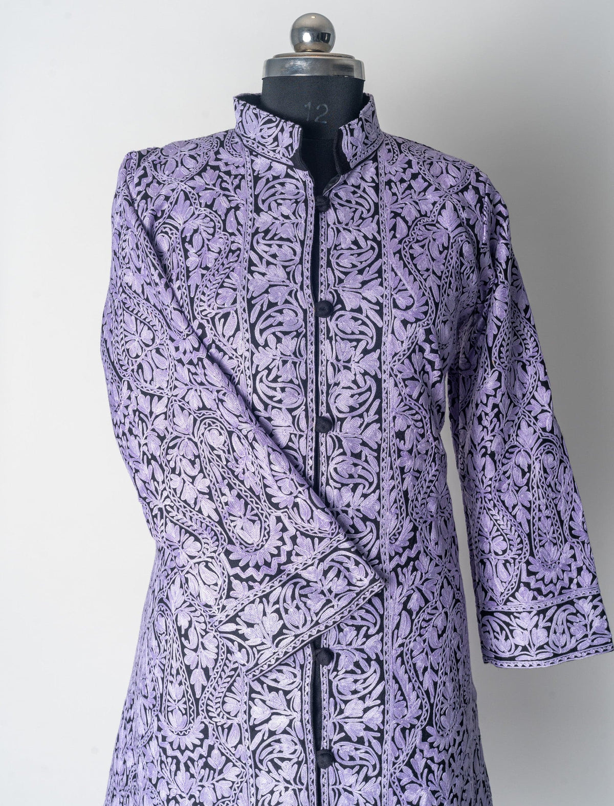 Upper front of the black wool jacket with pale lilac Aari embroidery, standing collar and one sleeve folded inward.