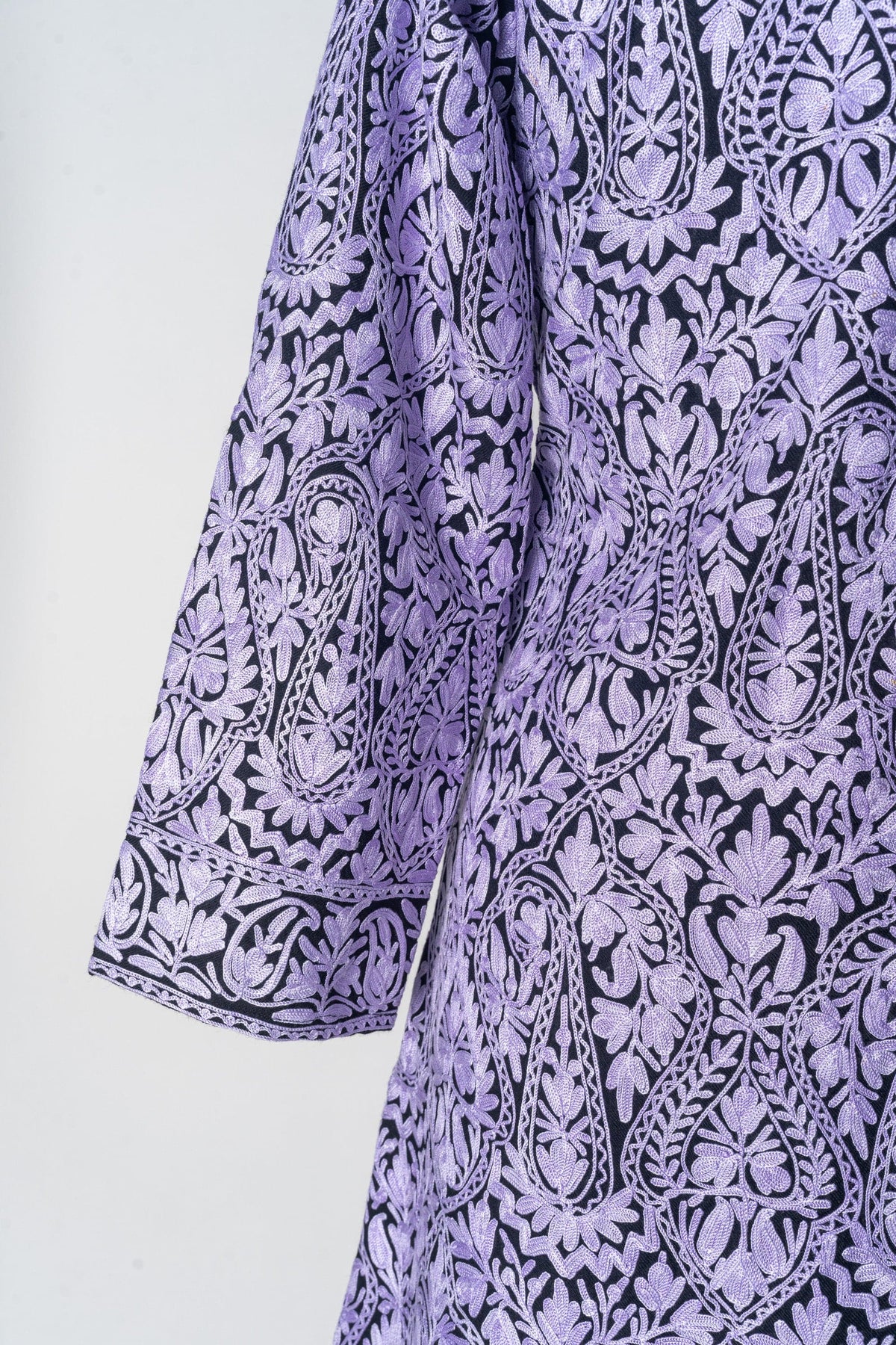 Detail of the black wool jacket’s sleeve and side, showing pale lilac Aari paisleys and a floral cuff border.