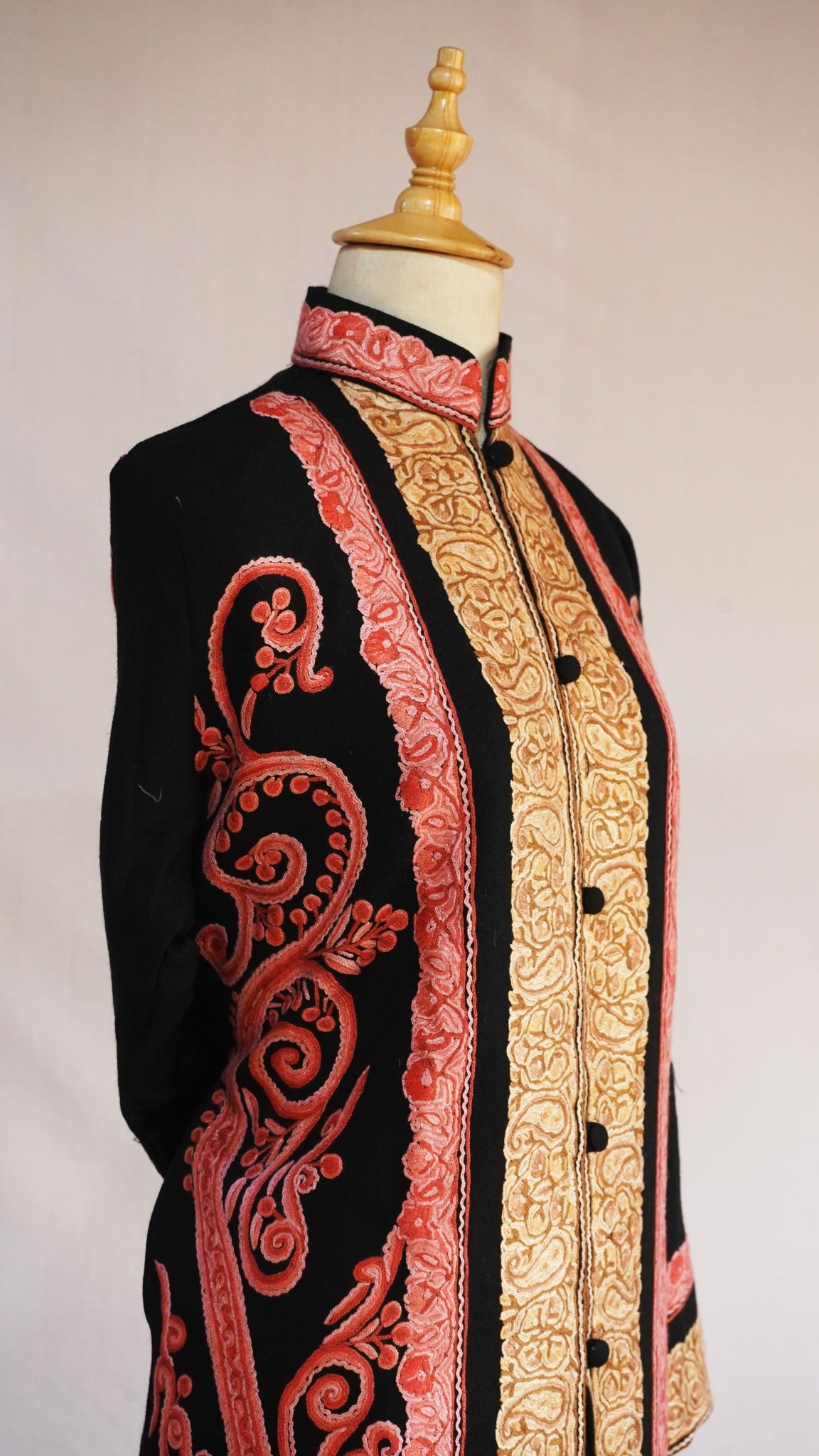 Close angled view of the black jacket’s stand collar and buttons, flanked by golden paisleys and coral-pink scrollwork