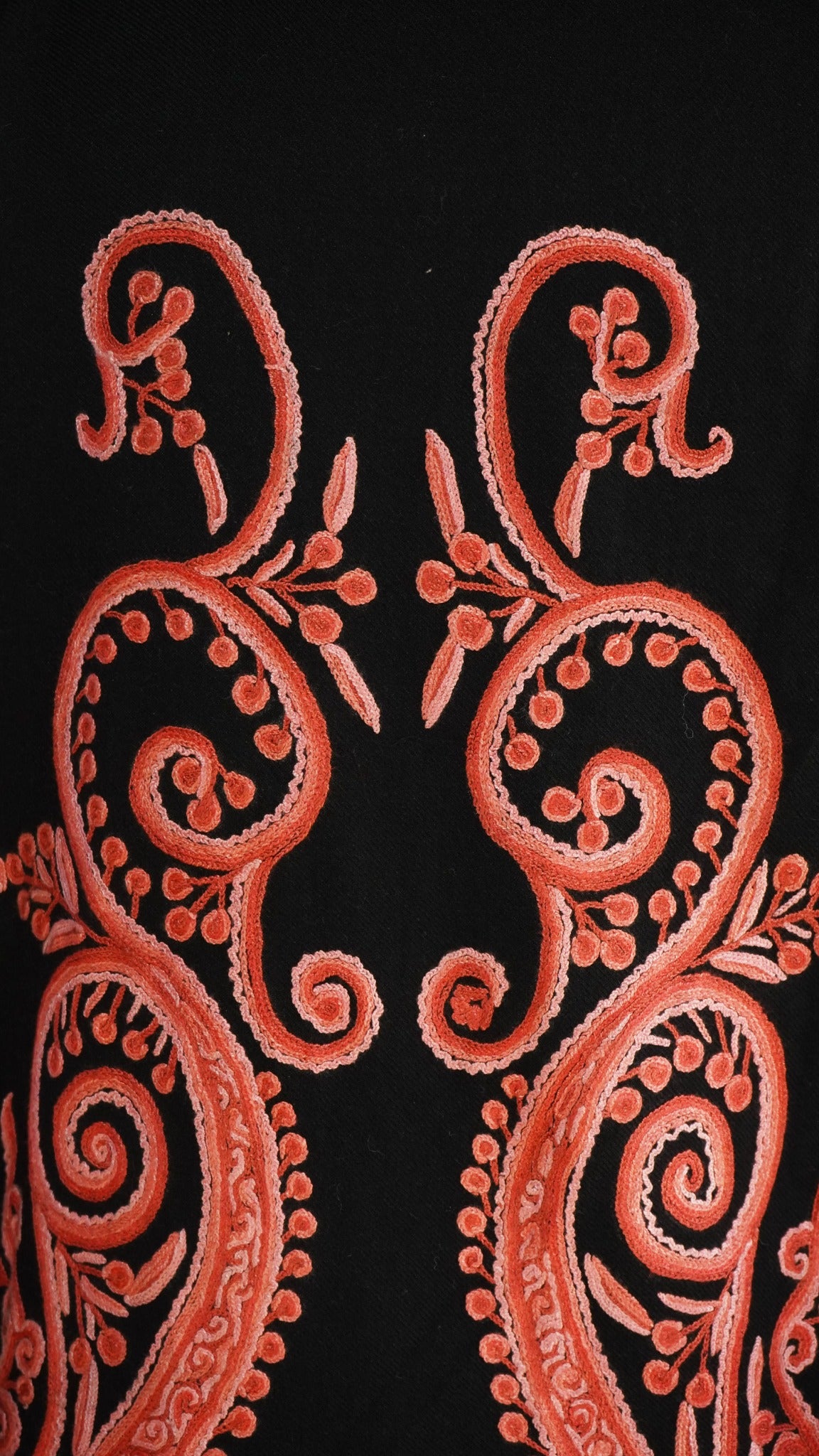 Close-up of paired coral-pink Aari scrolls and paisley curves on the black jacket’s back