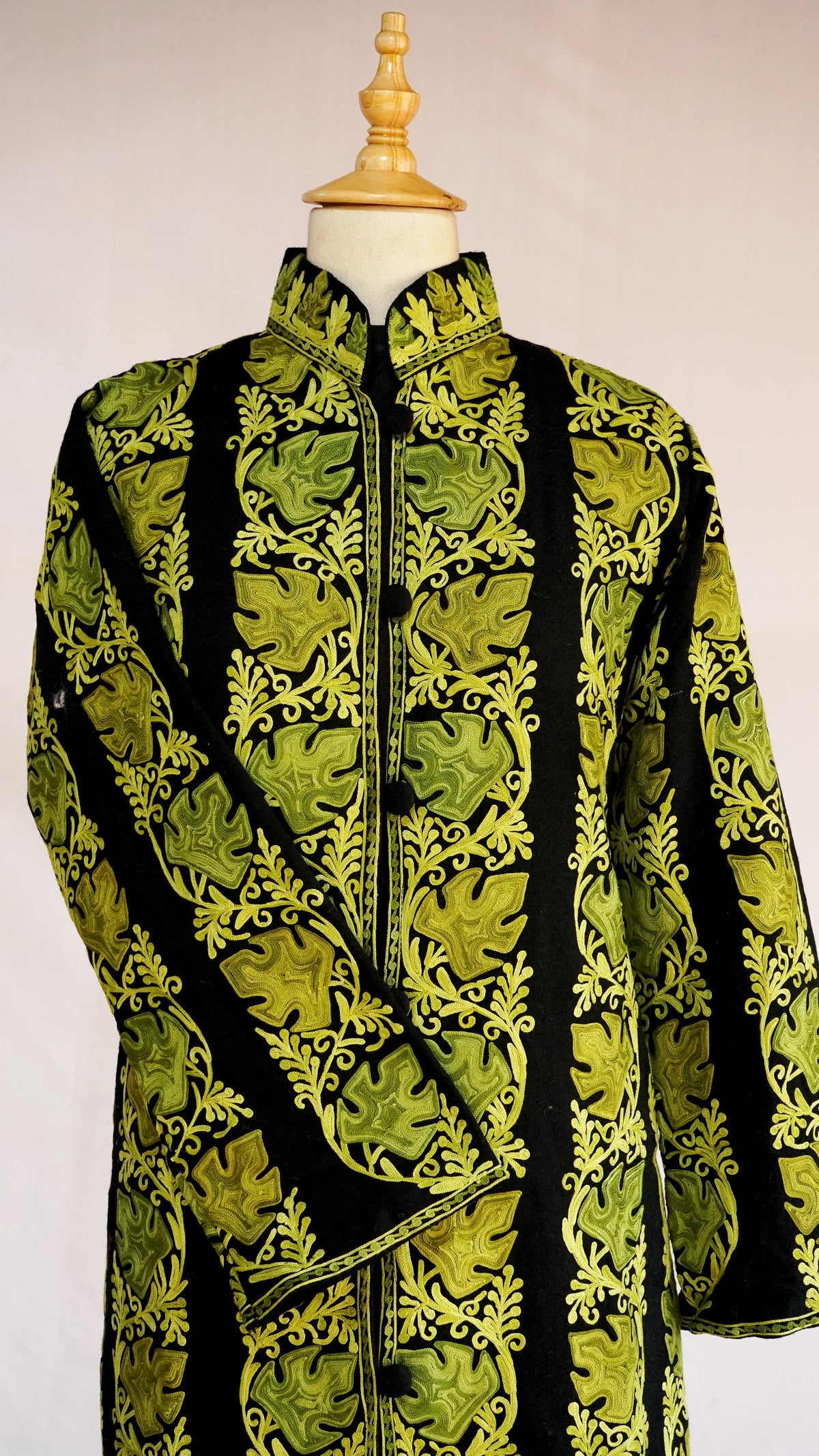 Upper front of a black jacket with one sleeve across the body, showing chartreuse leaf motifs and curling vines.