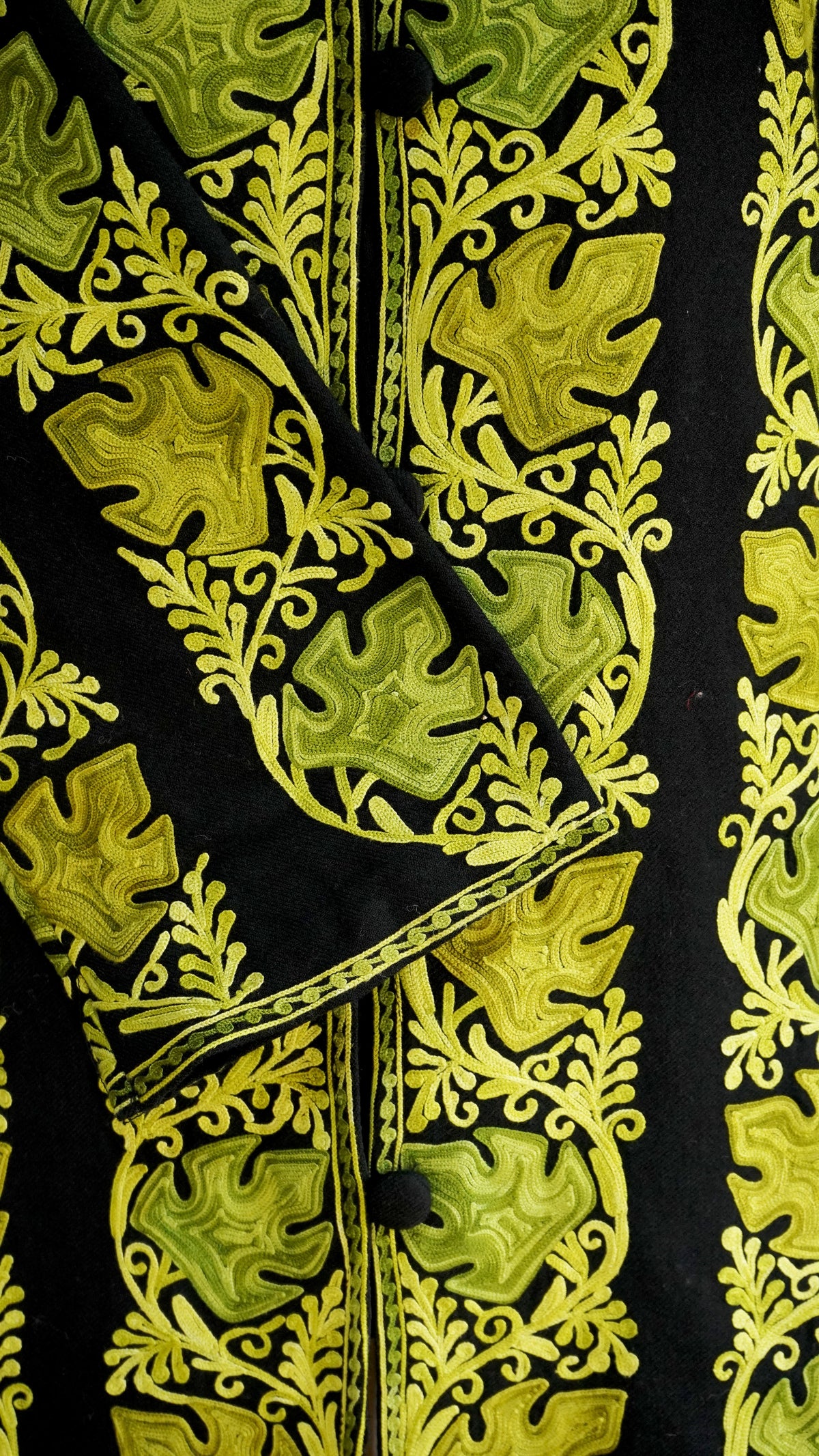 Detailed view of chartreuse leaf motifs and curling vines on the black jacket’s cuff and front.