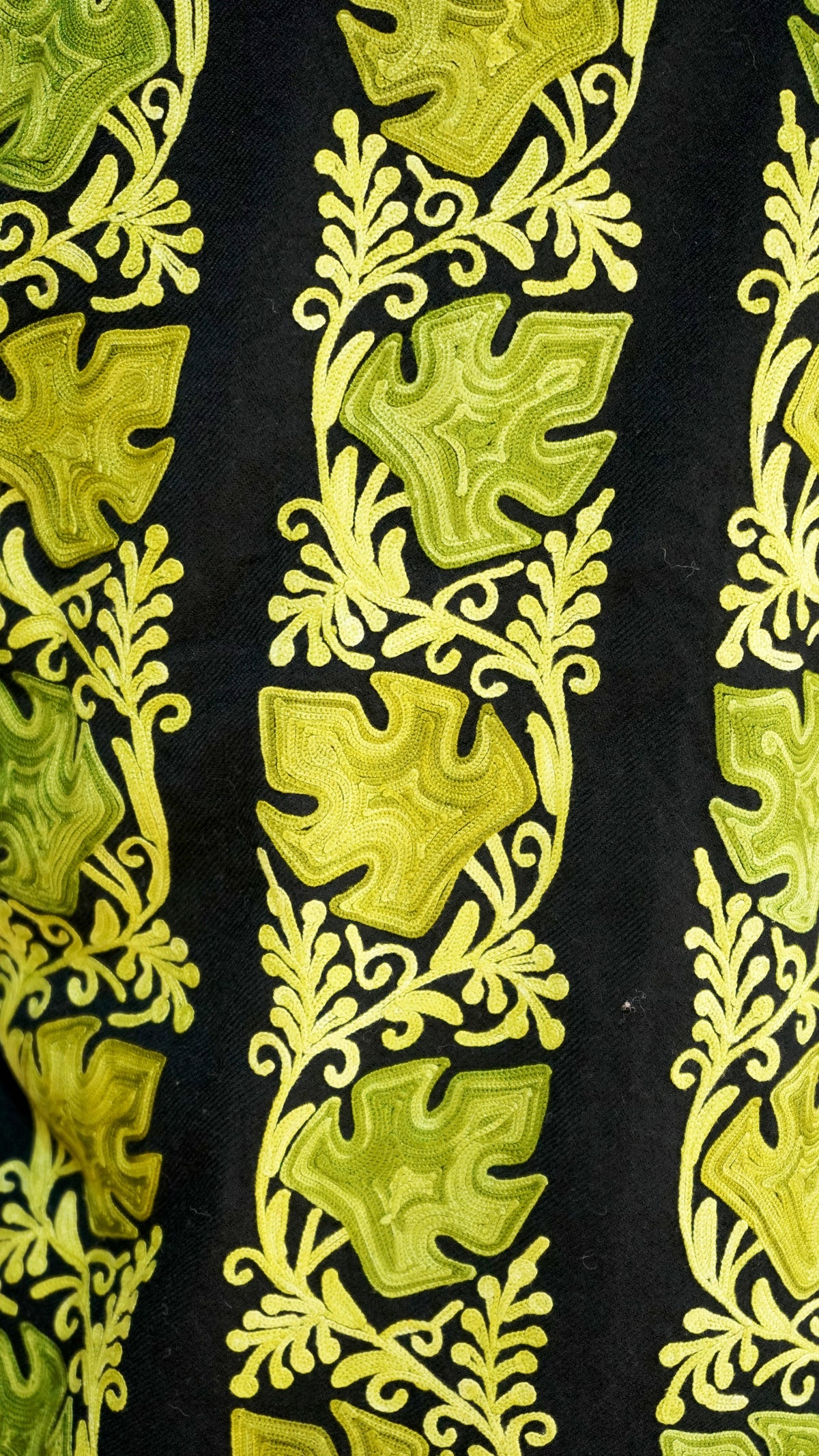 Close-up of chartreuse leaves and small curling floral vines embroidered in vertical bands on black fabric.
