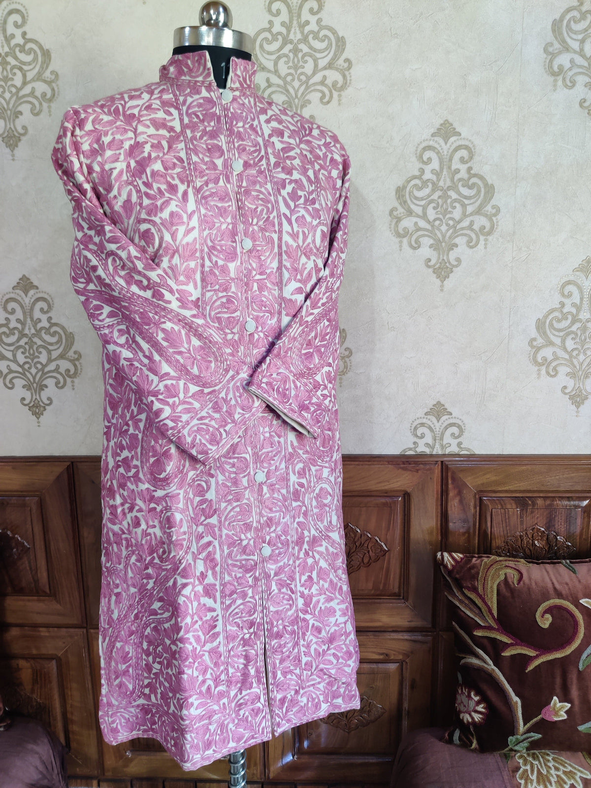 Angled front of a cream long jacket with dense pink Aari floral vines, a high collar and crossed sleeves