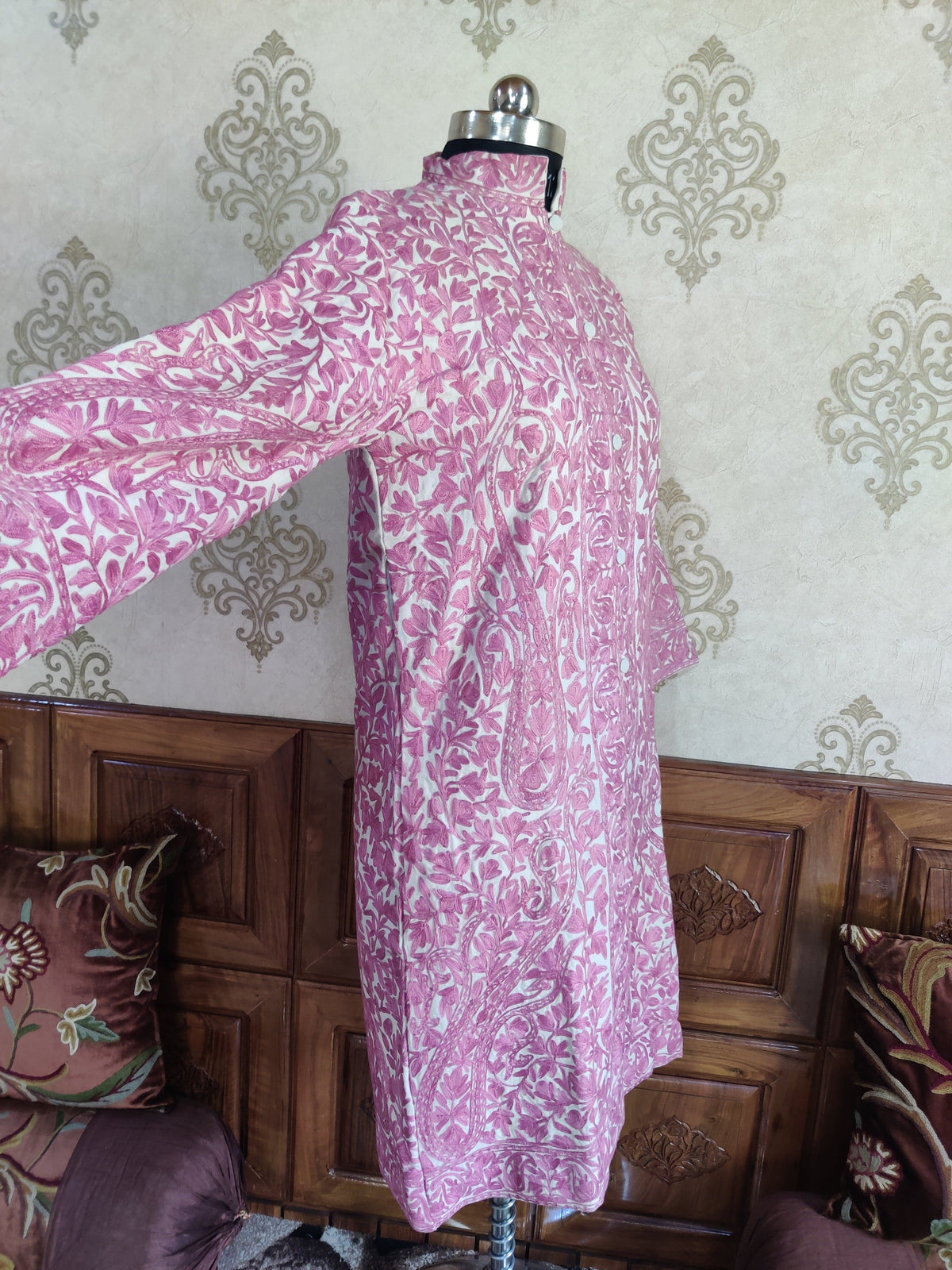 Side view of a cream jacket with dense pink Aari floral embroidery and one sleeve extended