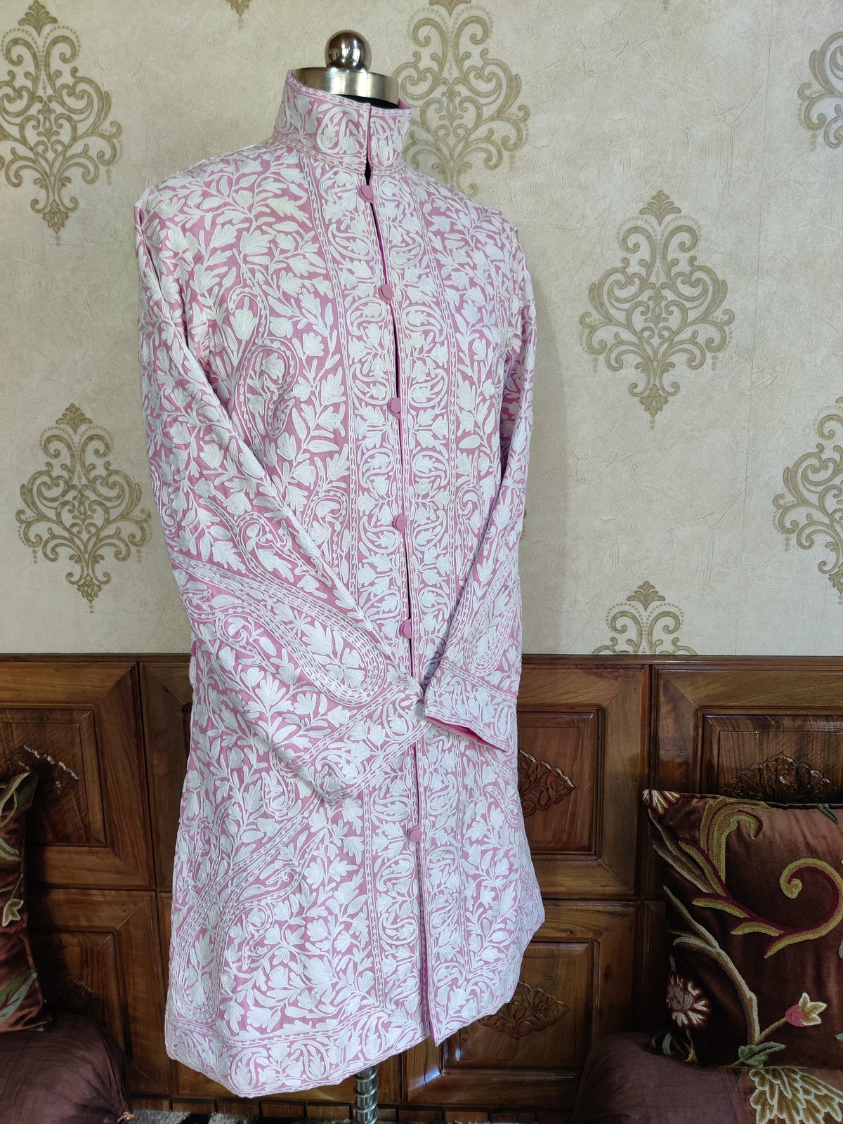 Full front view of a pale-pink jacket with crossed sleeves, white all-over embroidery and round covered buttons.