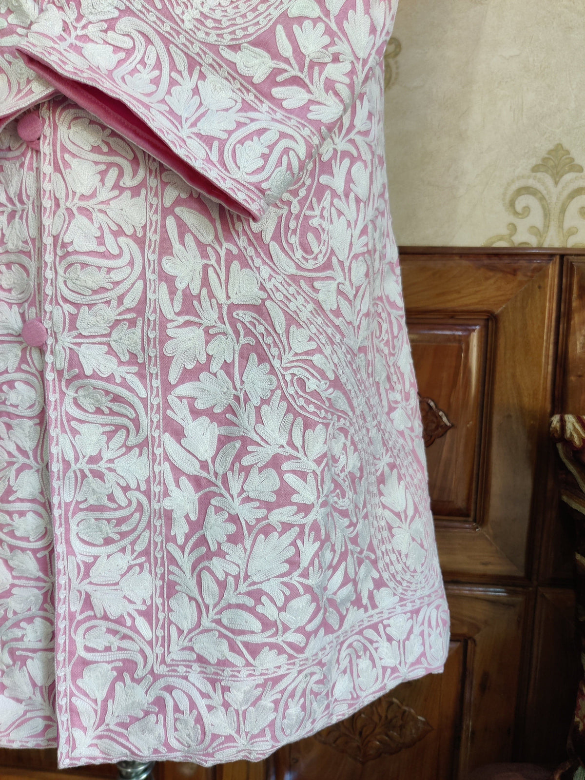 Lower front detail of the pink jacket showing white floral vines, an embroidered hem border and a patterned cuff.