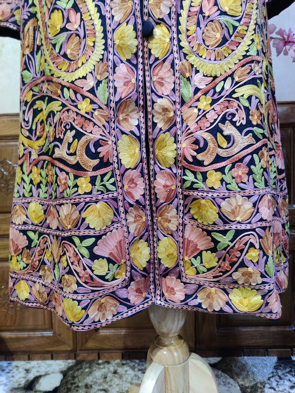 Lower front detail of a dark jacket with pink and yellow Aari floral bands and curling paisleys beside the buttoned opening