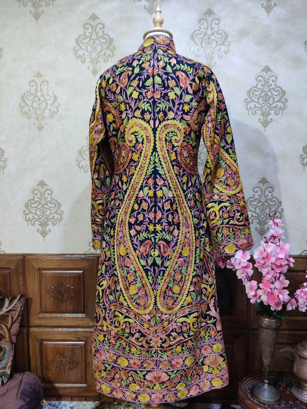 Back of a dark long jacket with two large symmetrical yellow-green Aari paisleys filled with pink and brown floral vines