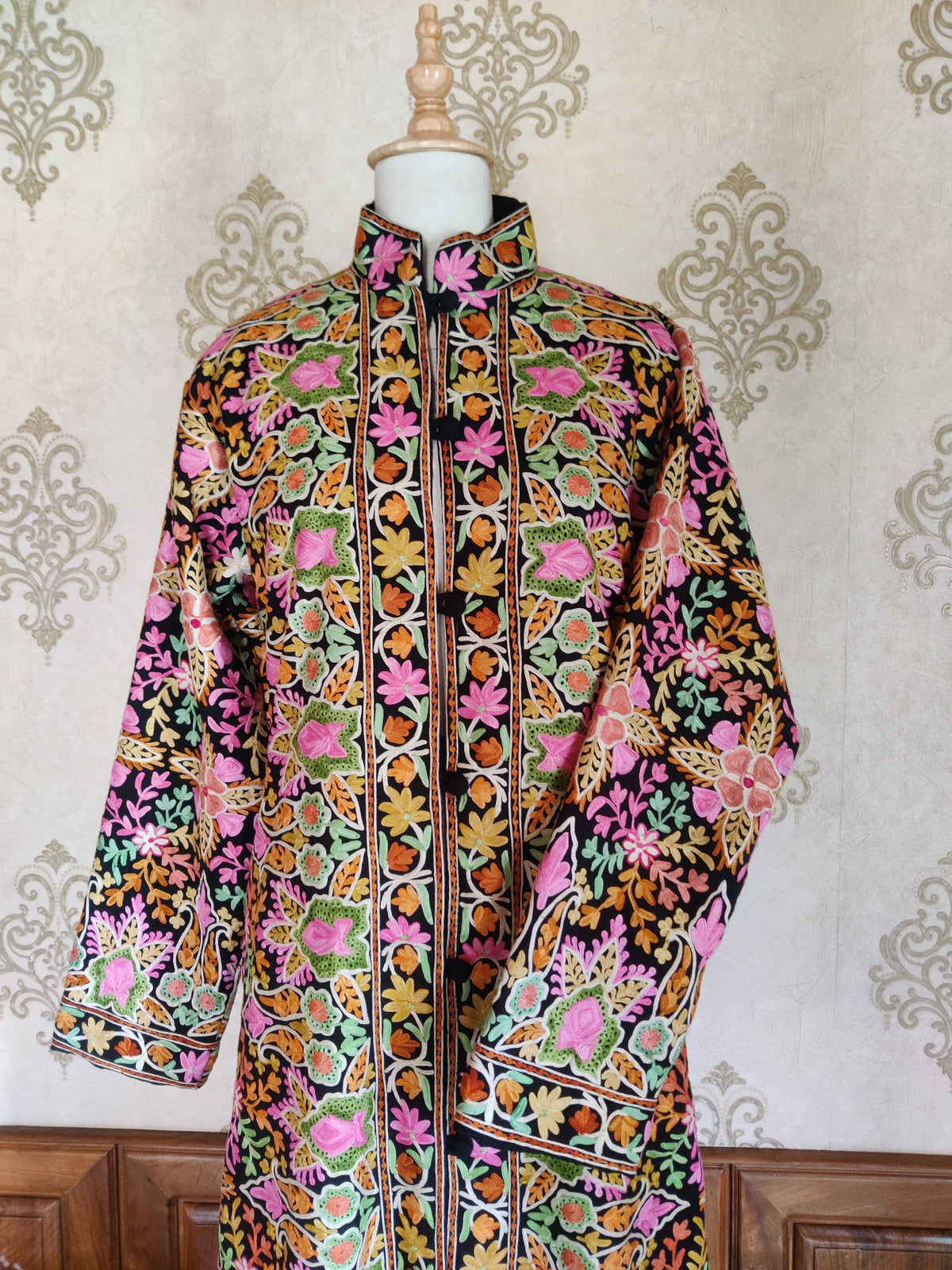 Upper front of a black Aari jacket with dense pink, orange, yellow and green floral embroidery and a stand collar