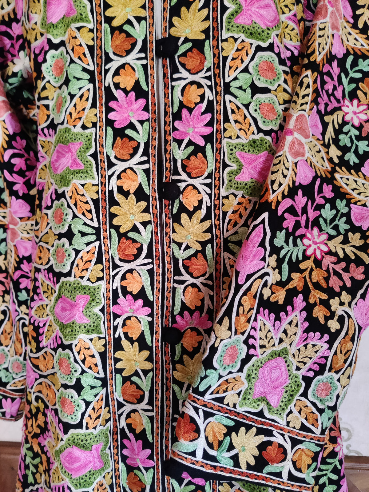 Black jacket front and folded cuff with bright Aari flowers, leafy motifs and narrow floral bands beside the buttons