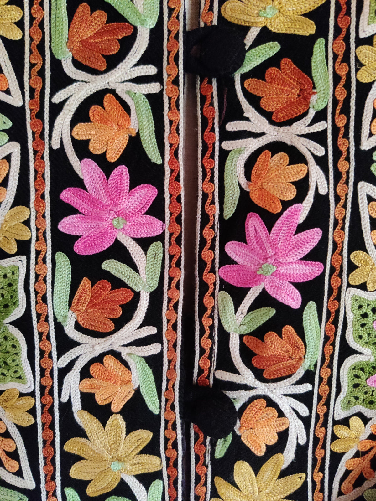 Close-up of pink, orange and yellow Aari flowers on white curling stems beside black covered buttons