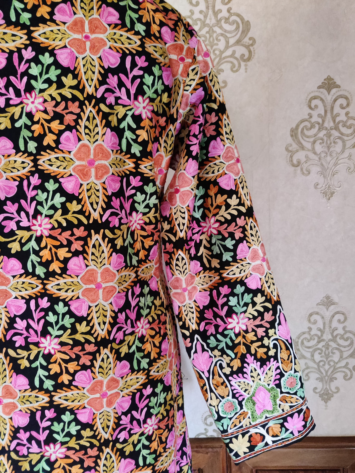 Back and sleeve detail of a black Aari jacket with pink-orange flowers, multicoloured leafy sprigs and an ornate cuff