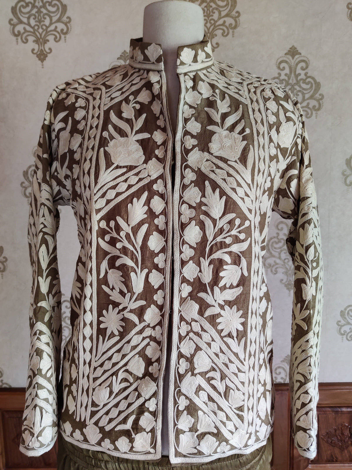 Front of the short brown jacket on a mannequin, with white Aari floral panels, standing collar and narrow white edging.