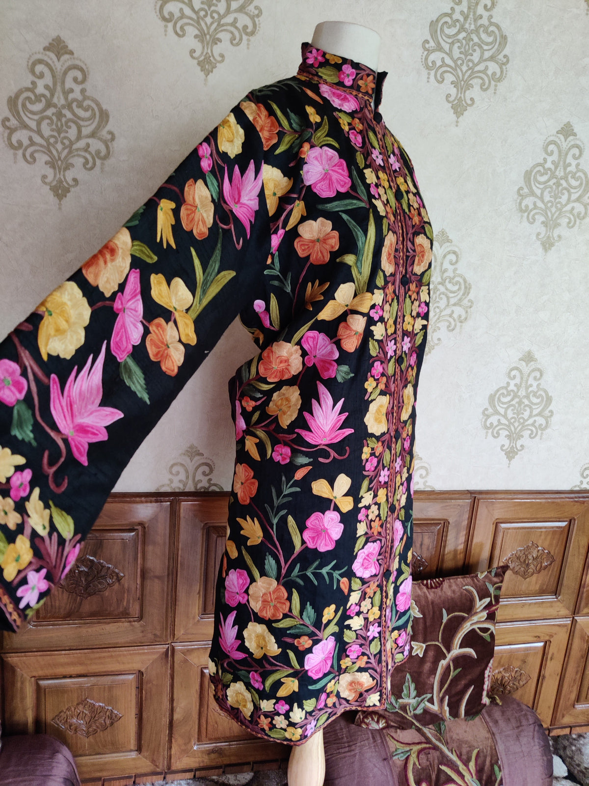 Side-front view of a black Aari jacket with one sleeve extended, showing large pink and yellow flowers and green leaves