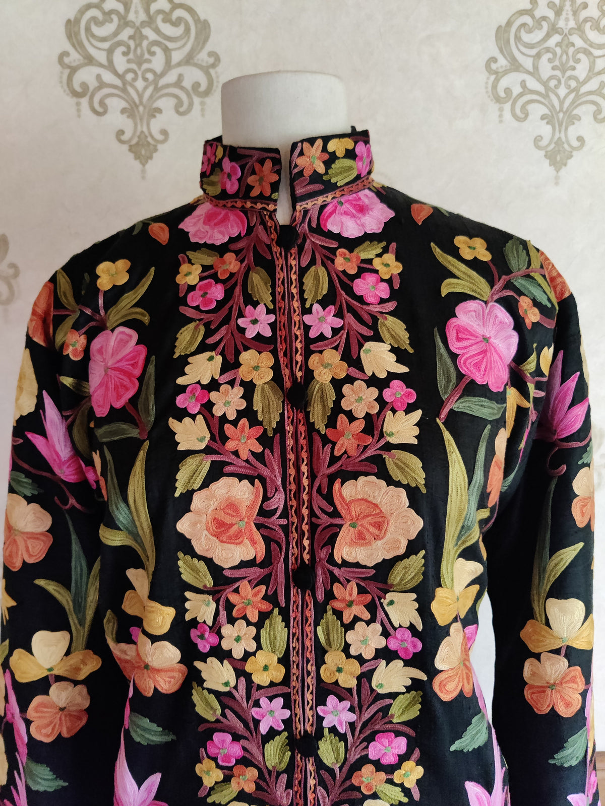 Upper front of a black Aari jacket with an embroidered stand collar and pink, peach and yellow flowers around the placket