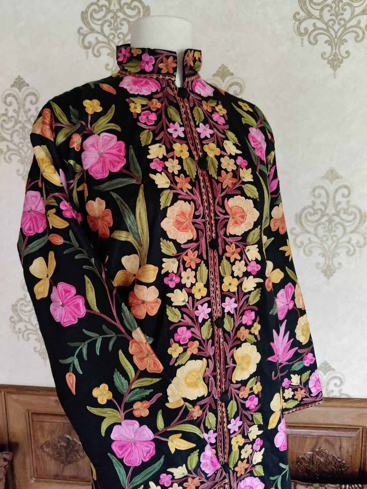 Angled upper view of a black Aari jacket with colourful floral vines, dense front panels and one sleeve across the waist