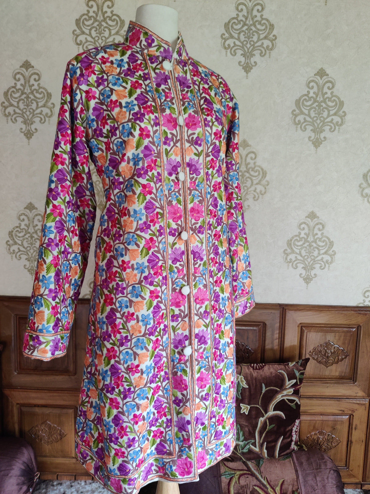 Angled full front of a white jacket with colourful Aari floral vines, a stand collar and white covered buttons