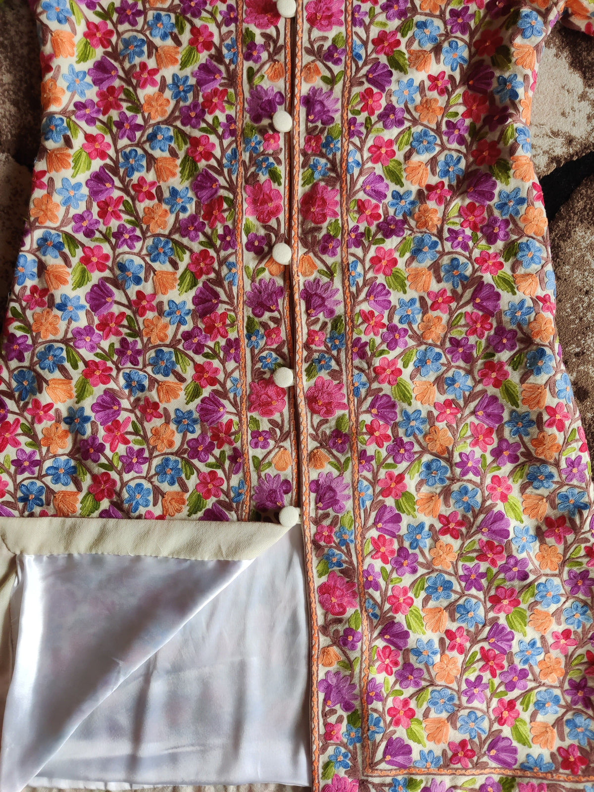 Lower front of the white floral jacket with the hem turned back to reveal pale lining beneath dense Aari embroidery