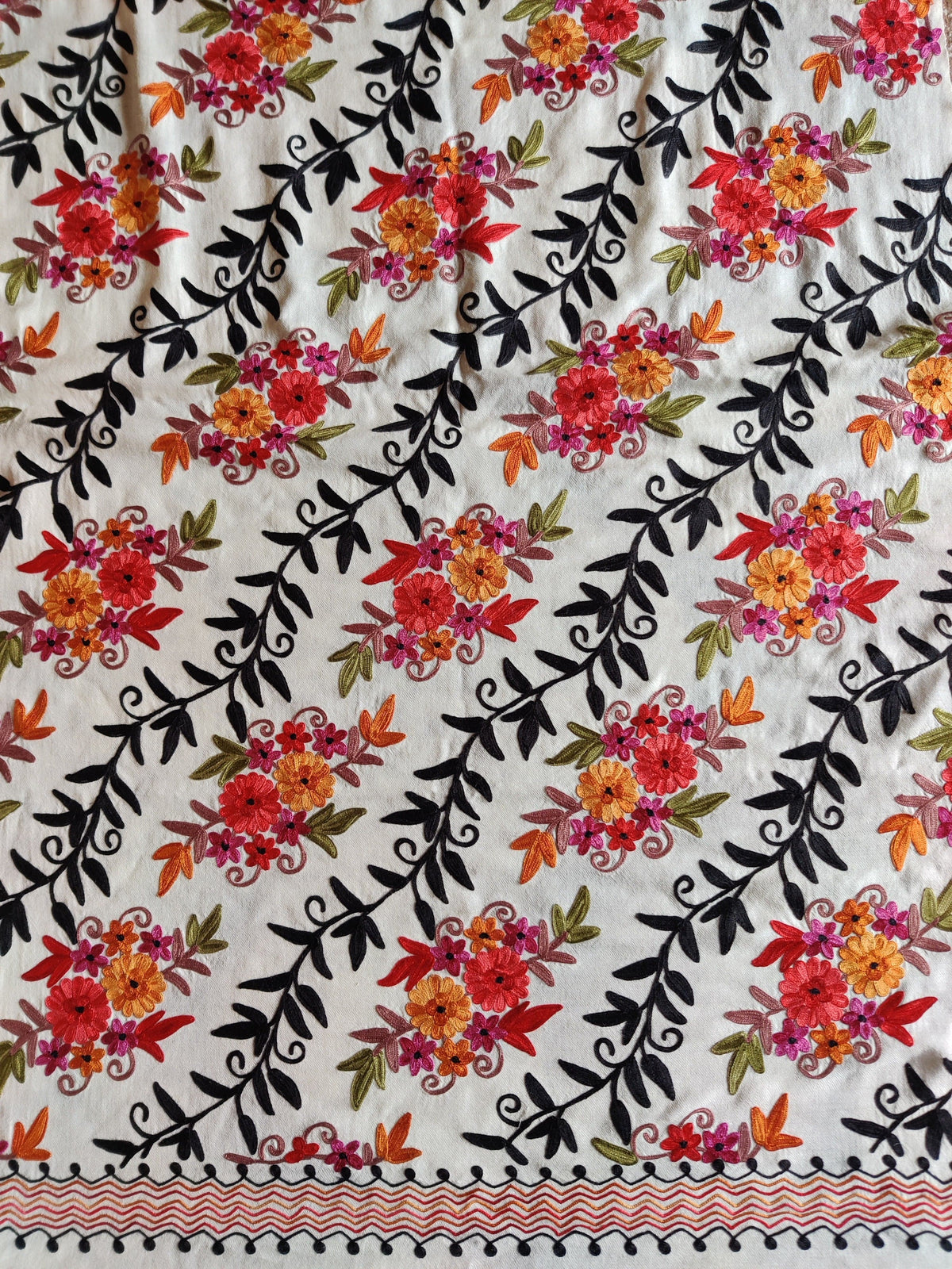 White merino wool stole laid flat, with rows of colourful Aari flower clusters and black leafy vines above a pink zigzag border.