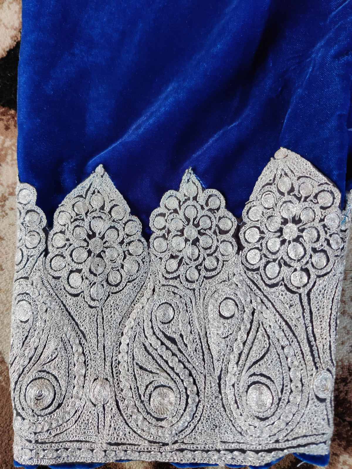 Close-up of the blue trouser ankle border with silver-toned paisleys and round floral motifs.