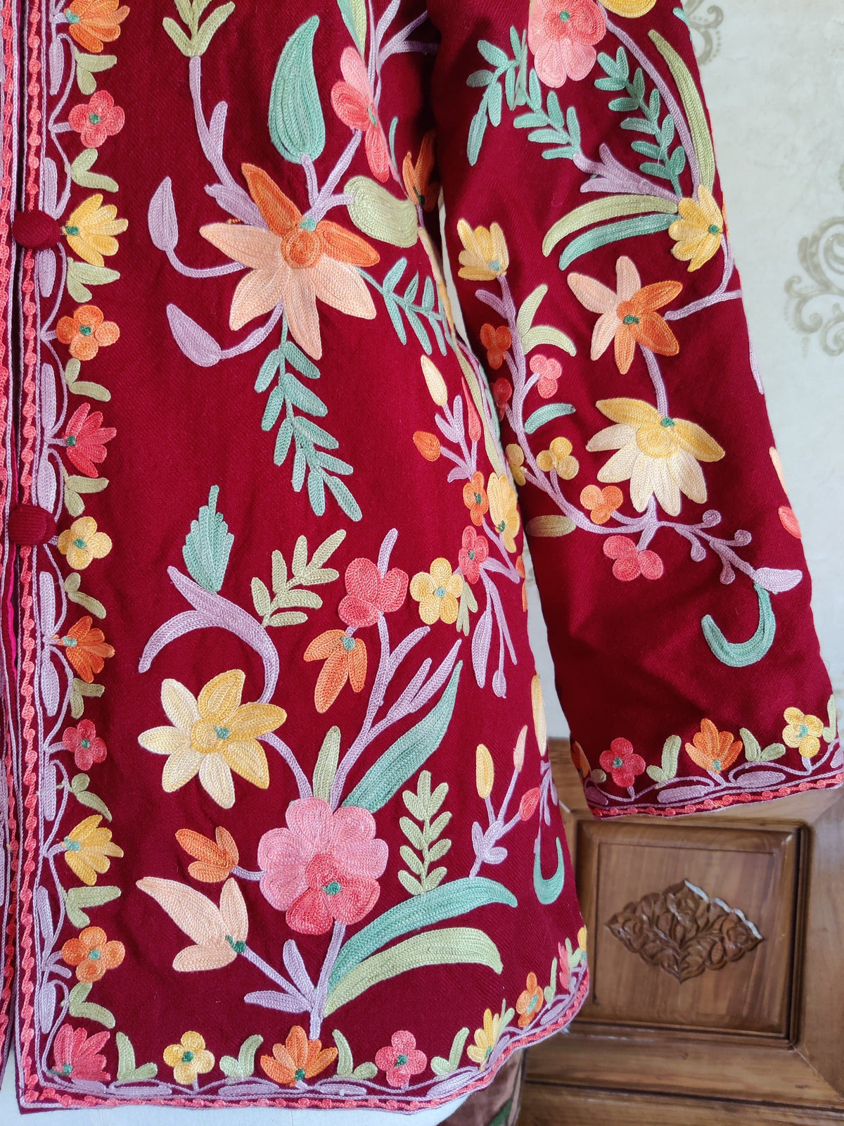Maroon jacket front and sleeve with pastel Aari flowers, mint leaves and a narrow floral border along the cuff and hem