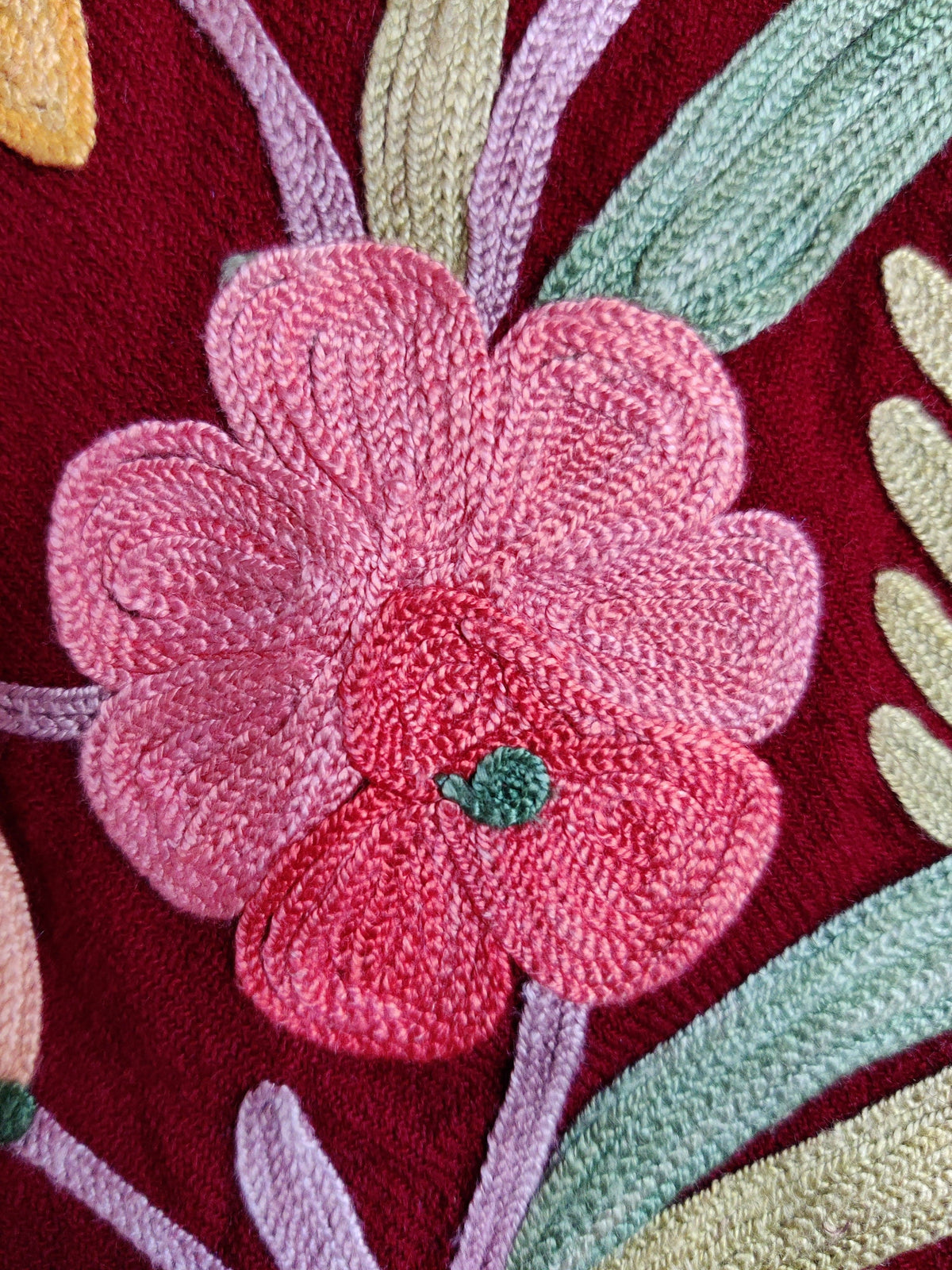 Macro view of a two-tone pink Aari flower with a green centre, lilac stem and mint leaves on maroon fabric